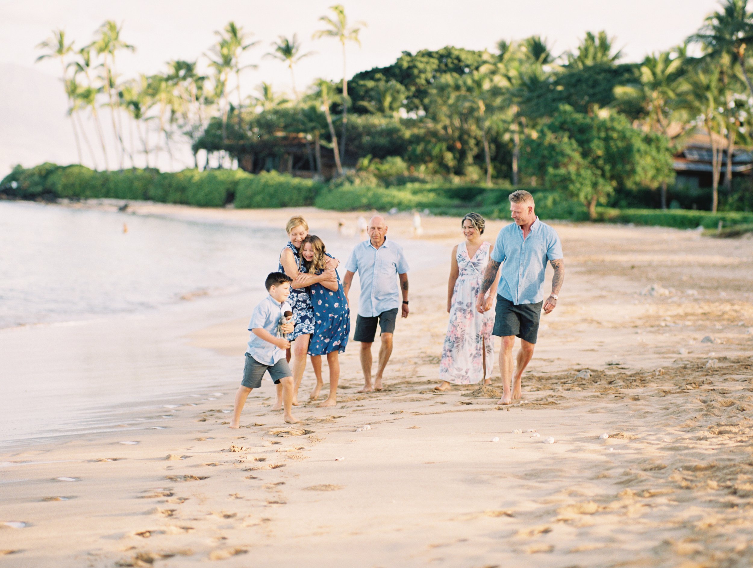 A family laughing while walking the shoreline of White Rock also known as Palauea Beach in Maui at sunrise.