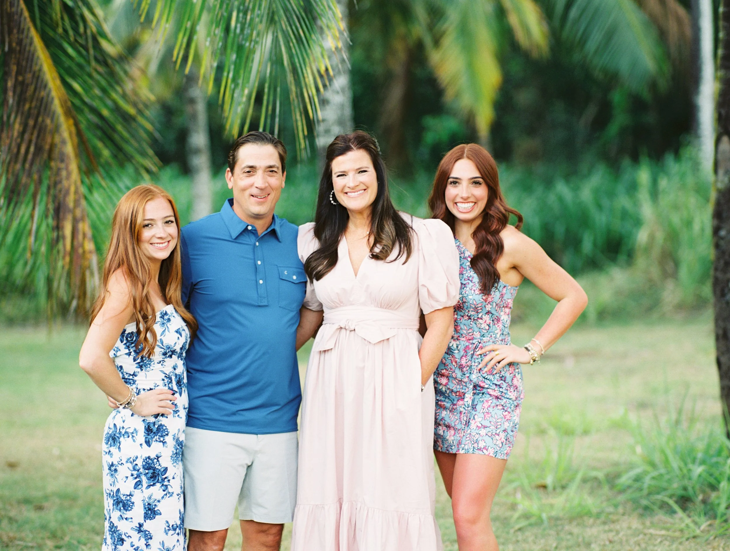 A family is standing under palm trees smiling during a morning Maui photoshoot in Wailea.