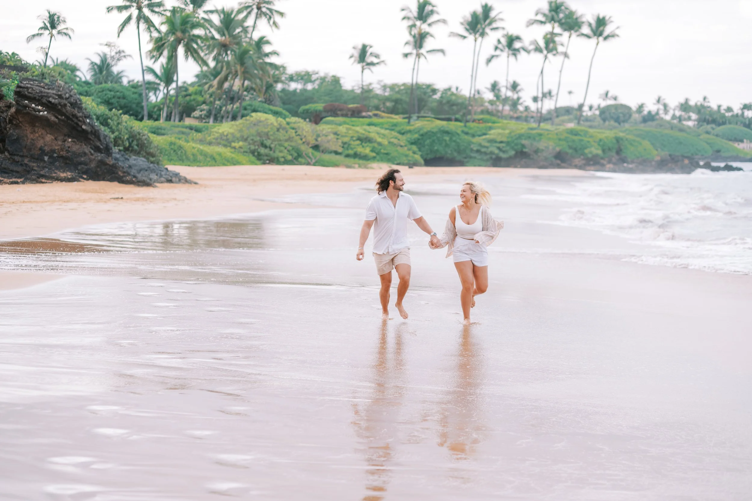 A couple running on the sand and through the water at Po'olenalena Beach in South Maui.