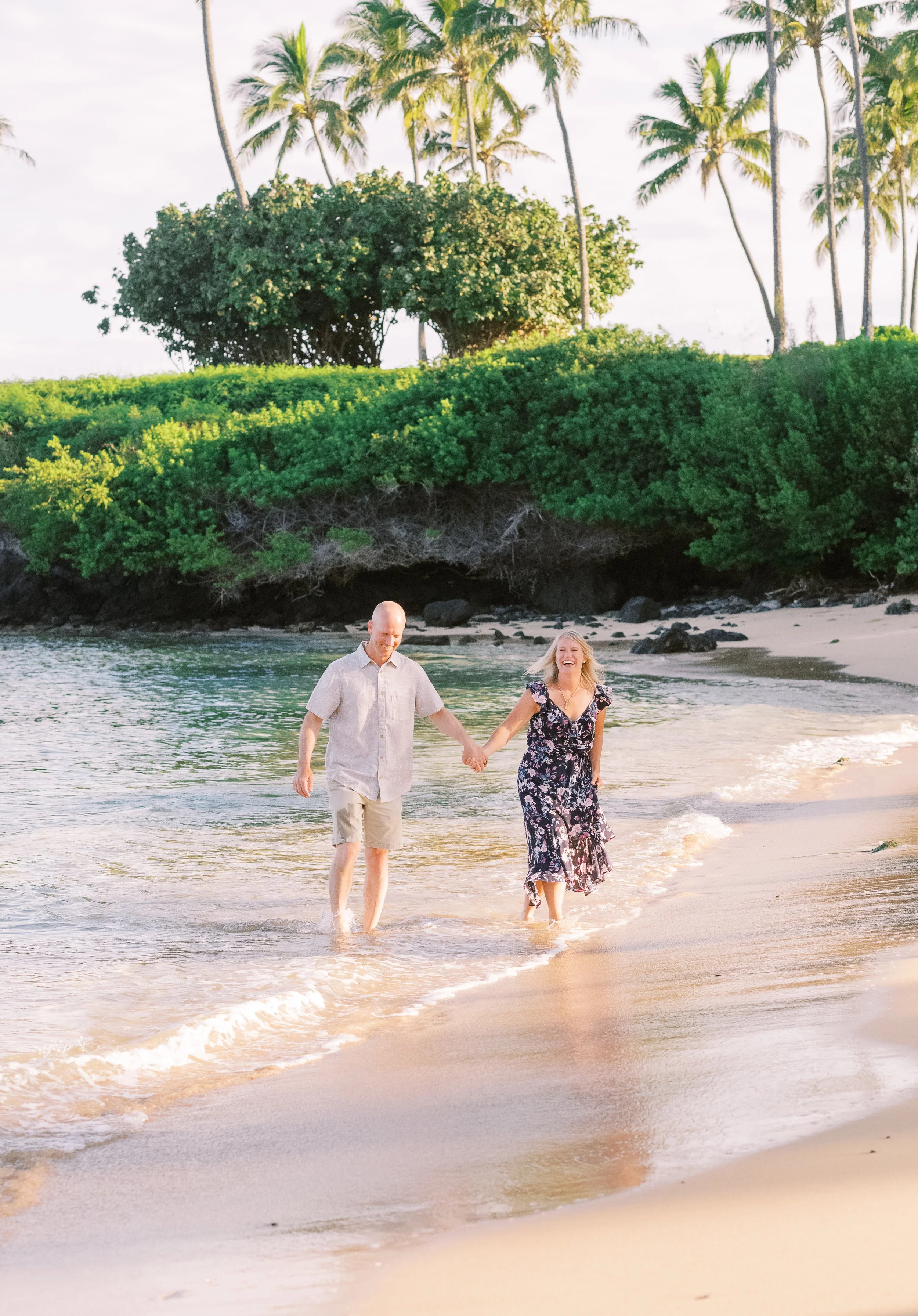 A couple laughing while walking on the beach at Kapalua Bay during sunrise in Maui Hawaii.