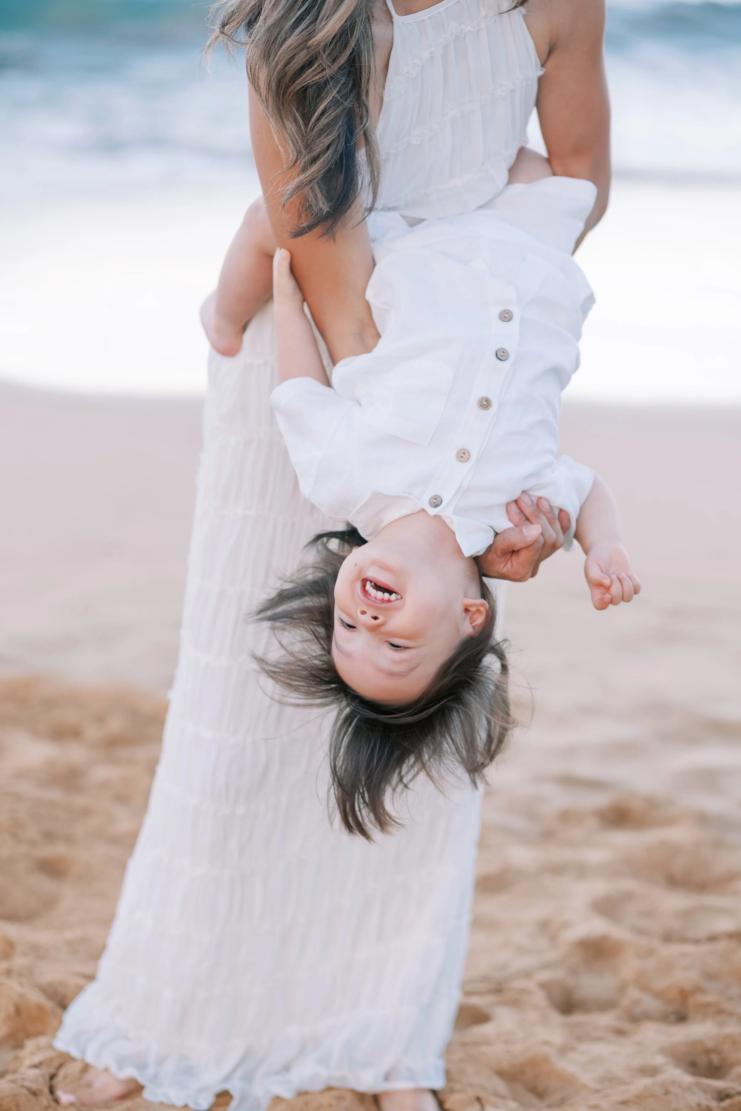 A toddler giggling upside down on Wailea Beach in Maui during a family sunrise photoshoot.