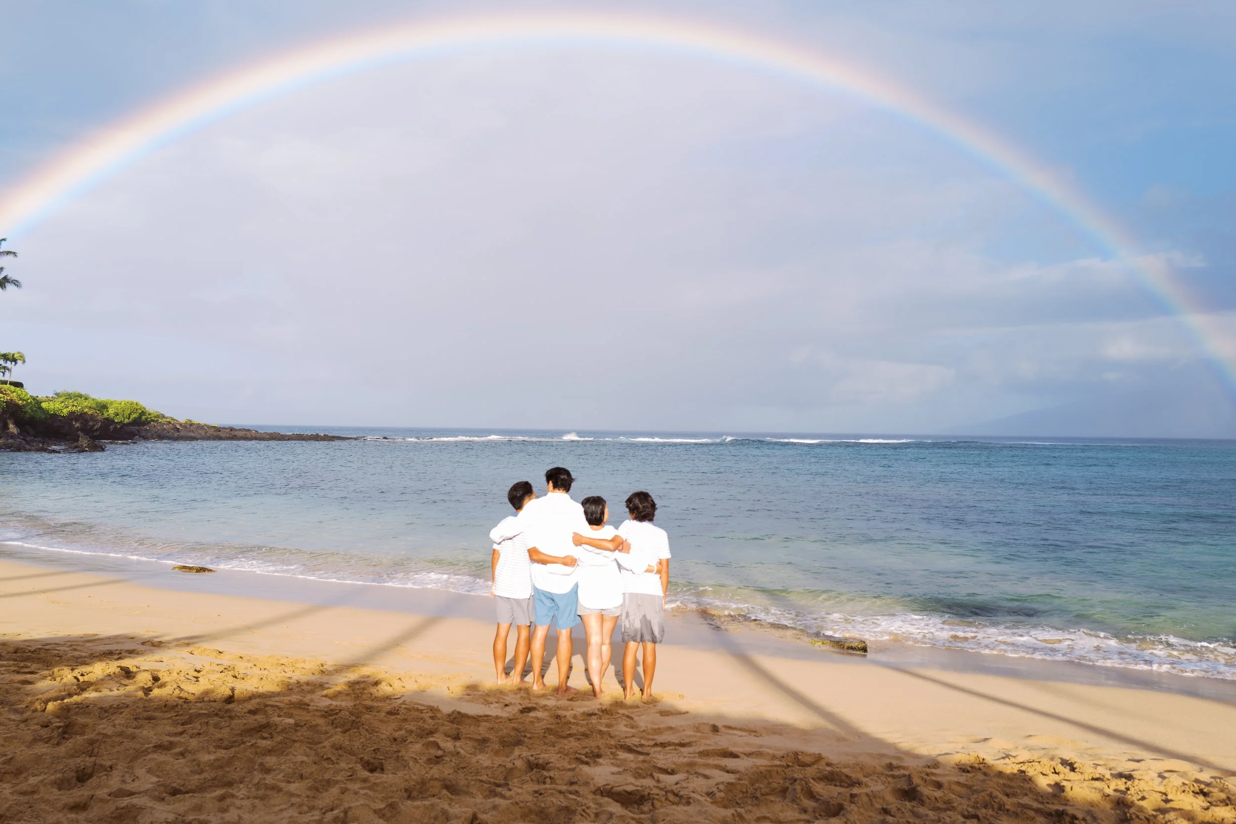 A family standing under a rainbow at Kapalua Bay Maui during a family photoshoot.