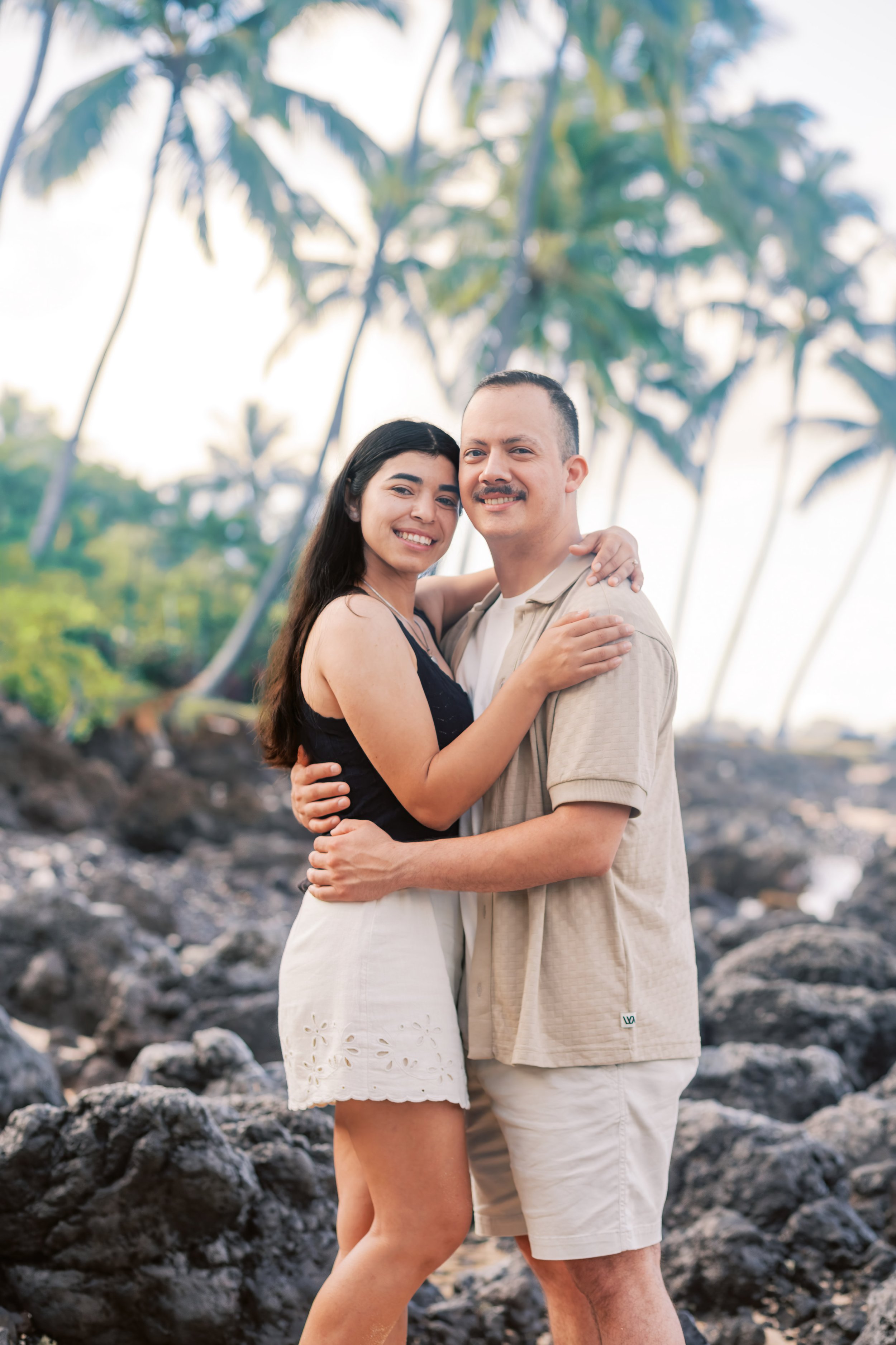 A surprise proposal at Makena Cove in Maui with a couple warmly embracing underneath the palm trees while standing on the beach.