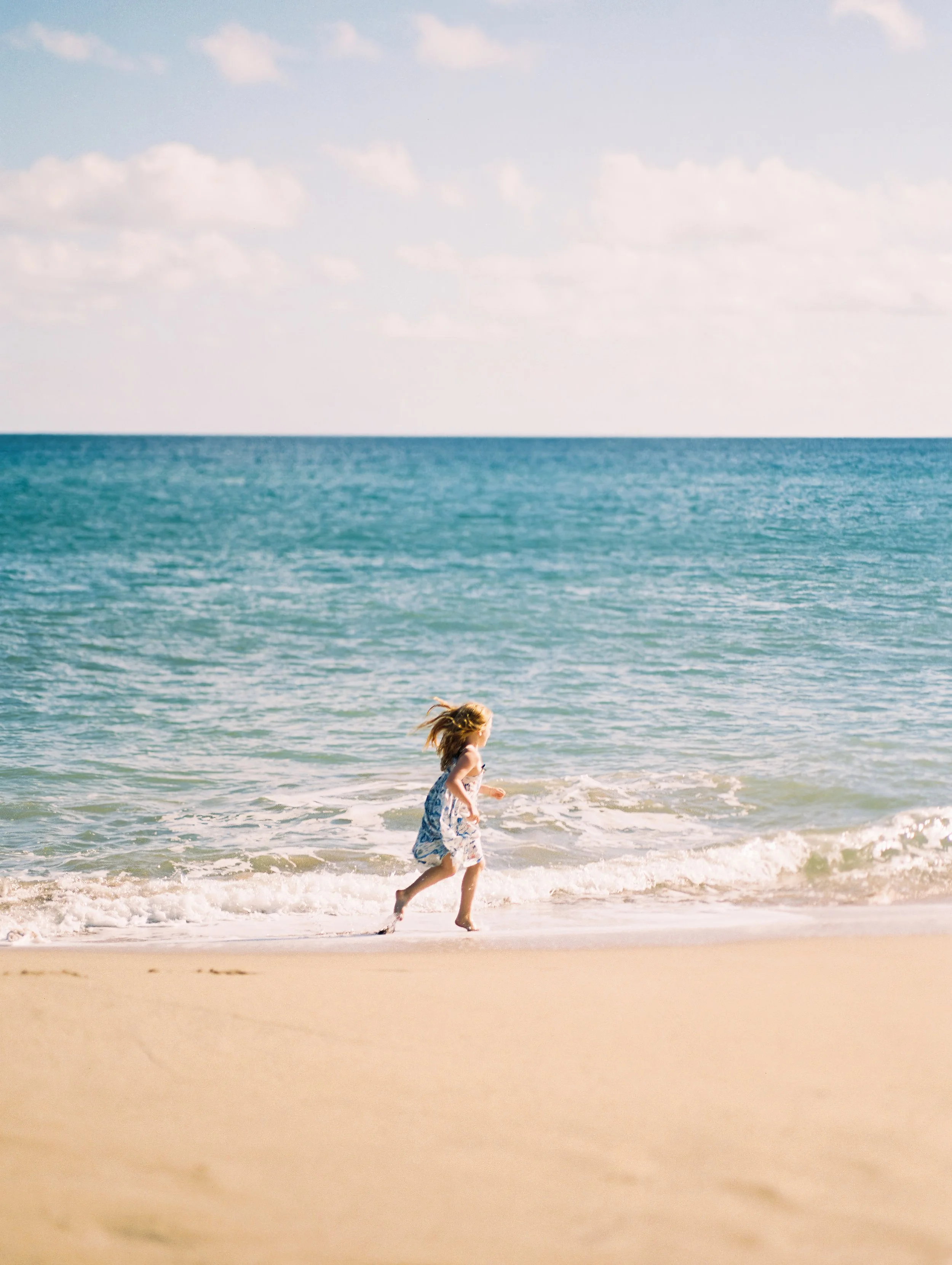 A little girl running on the beach next to bright blue tropical water in Maui Hawaii captured on film.