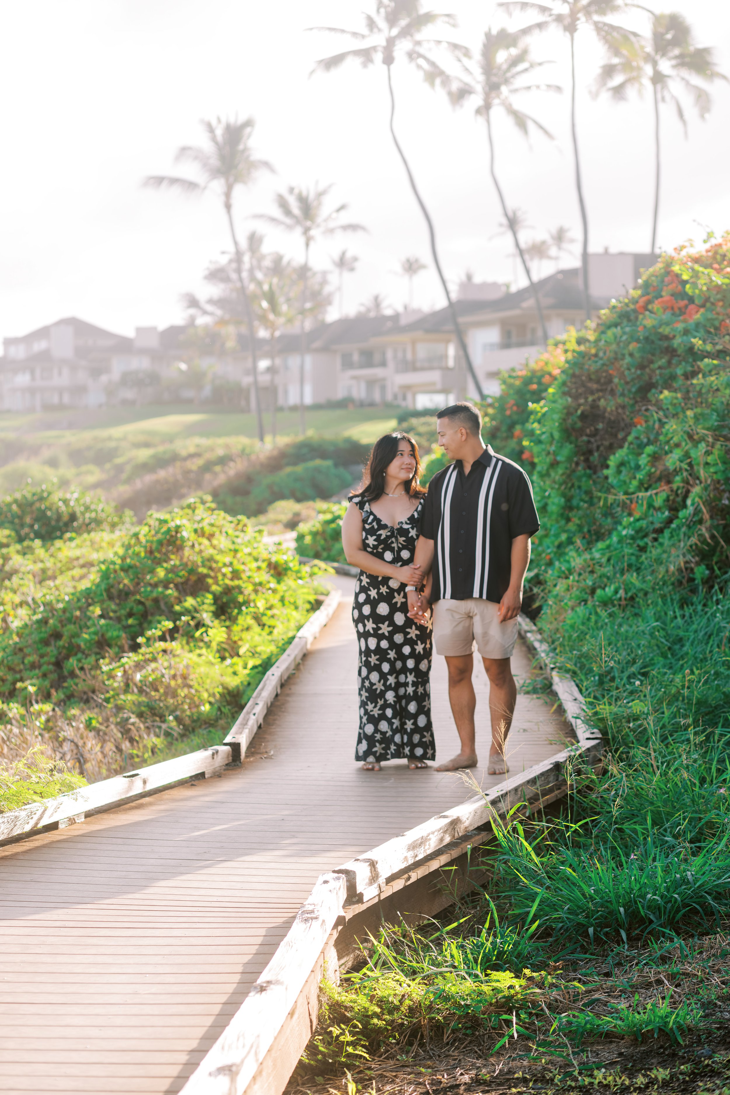 A couple walking the boardwalk of Ironwoods Beach with palm trees behind them in the early morning light.