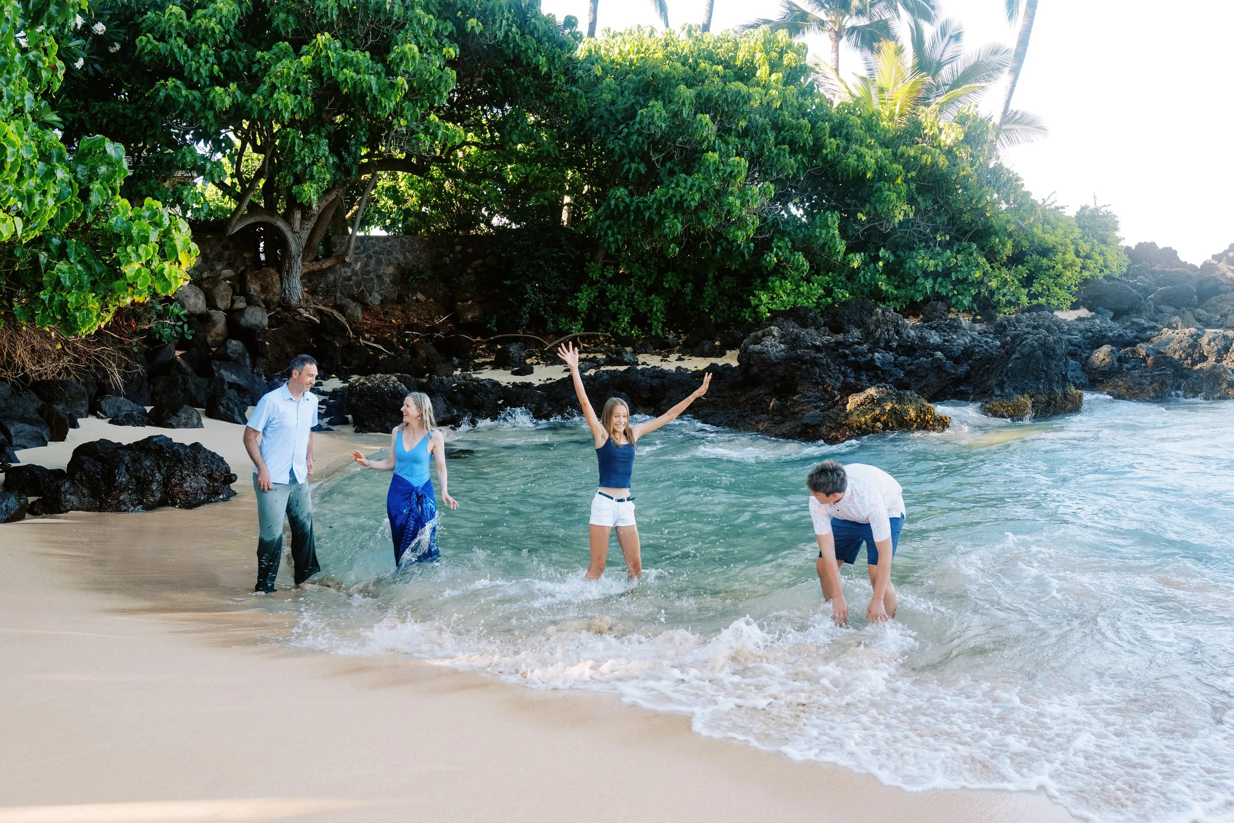 A family splashing and playing in the ocean during a family photoshoot at Makena Cove on Maui.