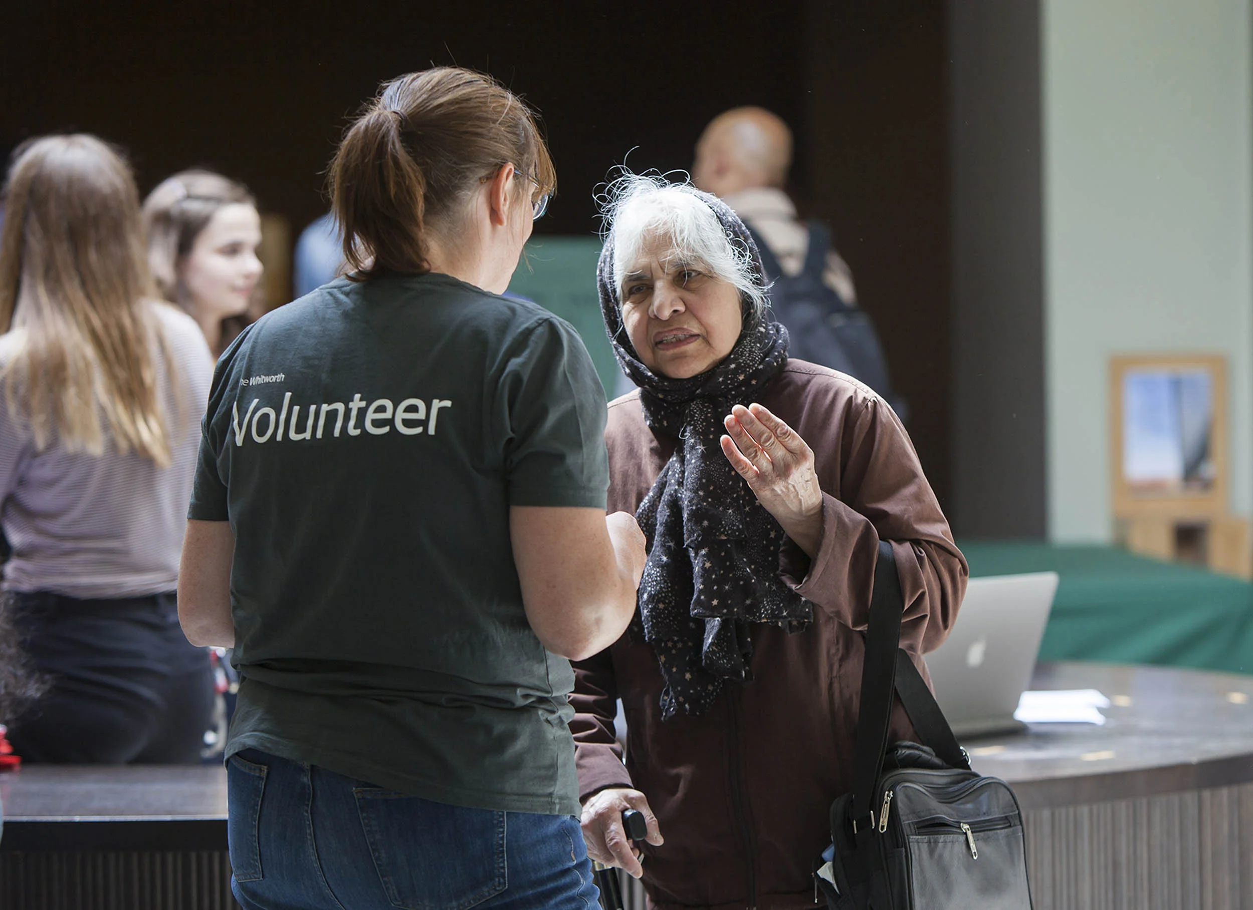 A documentary photograph of the a volunteer speaking to a visitor at an event. Photography commissioned by Whitworth Art Gallery, Manchester