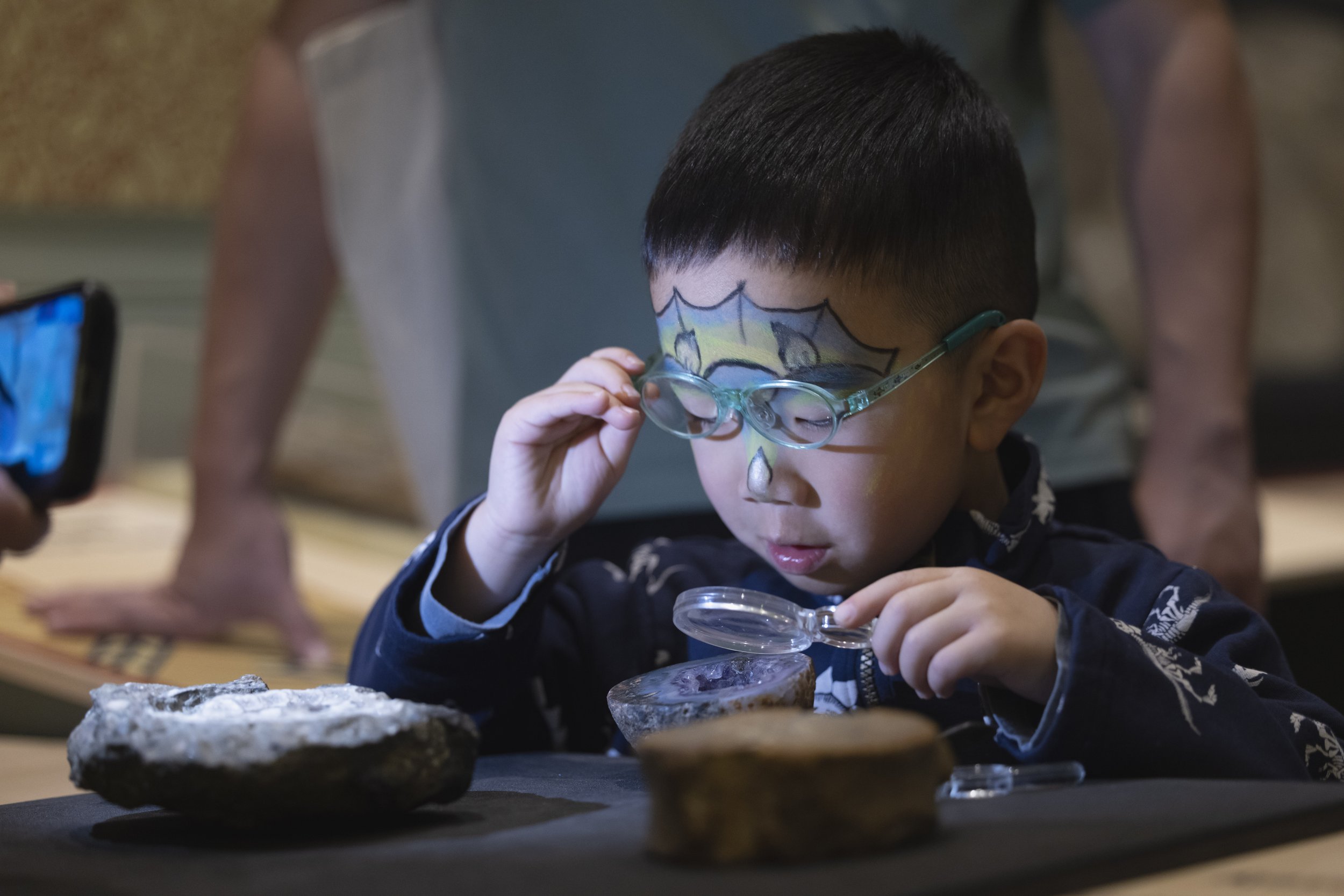  Young Asian boy with glasses using a magnifying glass to examine an exhibit during a public event at Manchester Museum. 