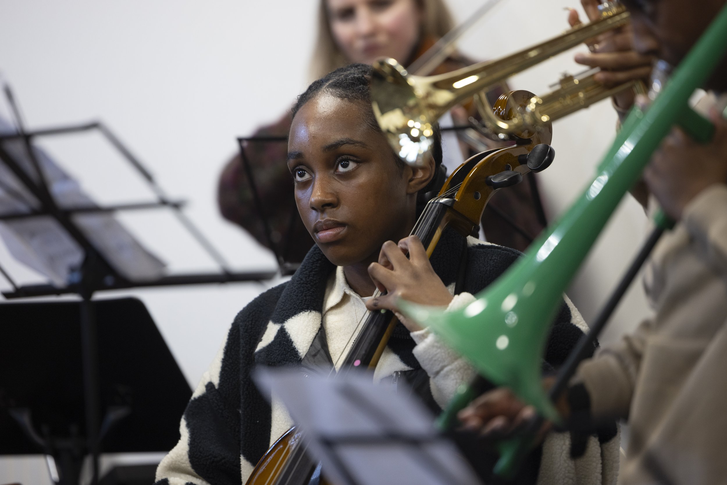   Girl playing cello while looking at conductor during Olympias Music Foundation concert, Manchester – documentary photography by David Oates  