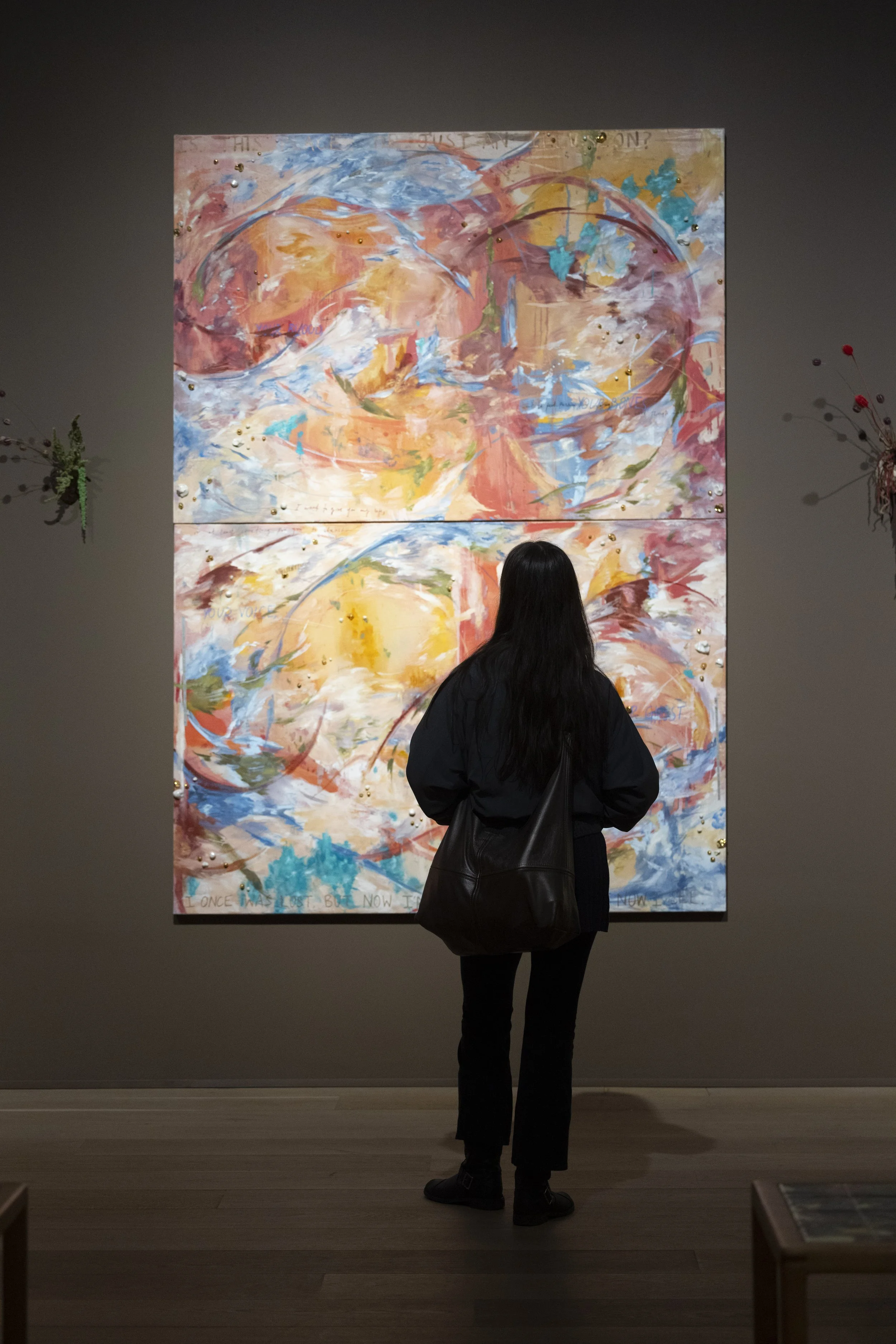 Young woman silhouetted against large colourful abstract canvas in gallery space.