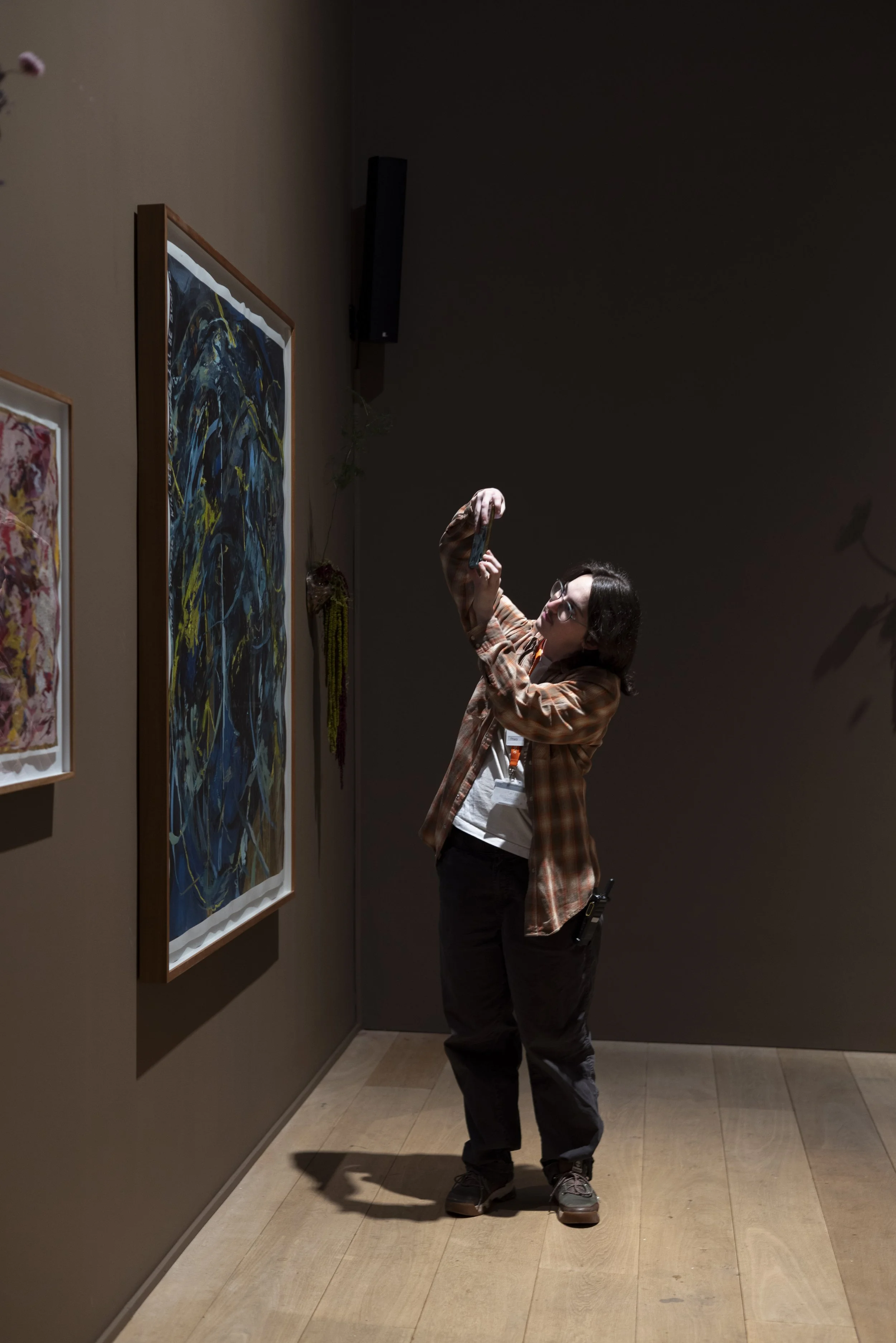 Visitor photographing gallery canvas artwork on smartphone during exhibition opening.