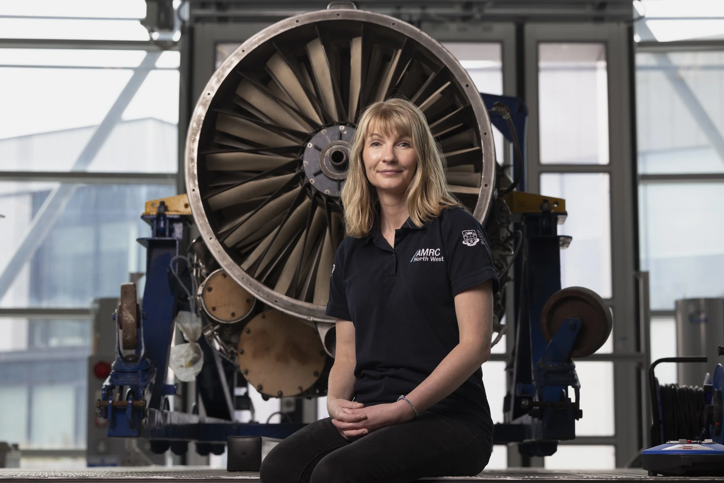 Kristina Parry seated in front of a large gas turbine engine fan in an industrial research environment, environmental portrait photography for UK innovation and engineering sector editorial feature