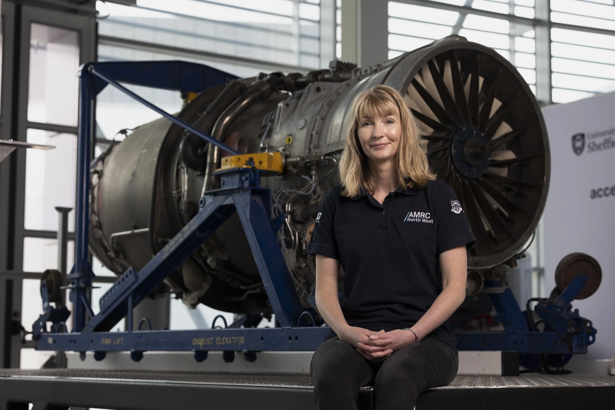 Kristina Parry in three-quarter view standing in front of a large gas turbine engine fan within an industrial research facility, editorial portrait photography for Connected Places Catapult innovation feature