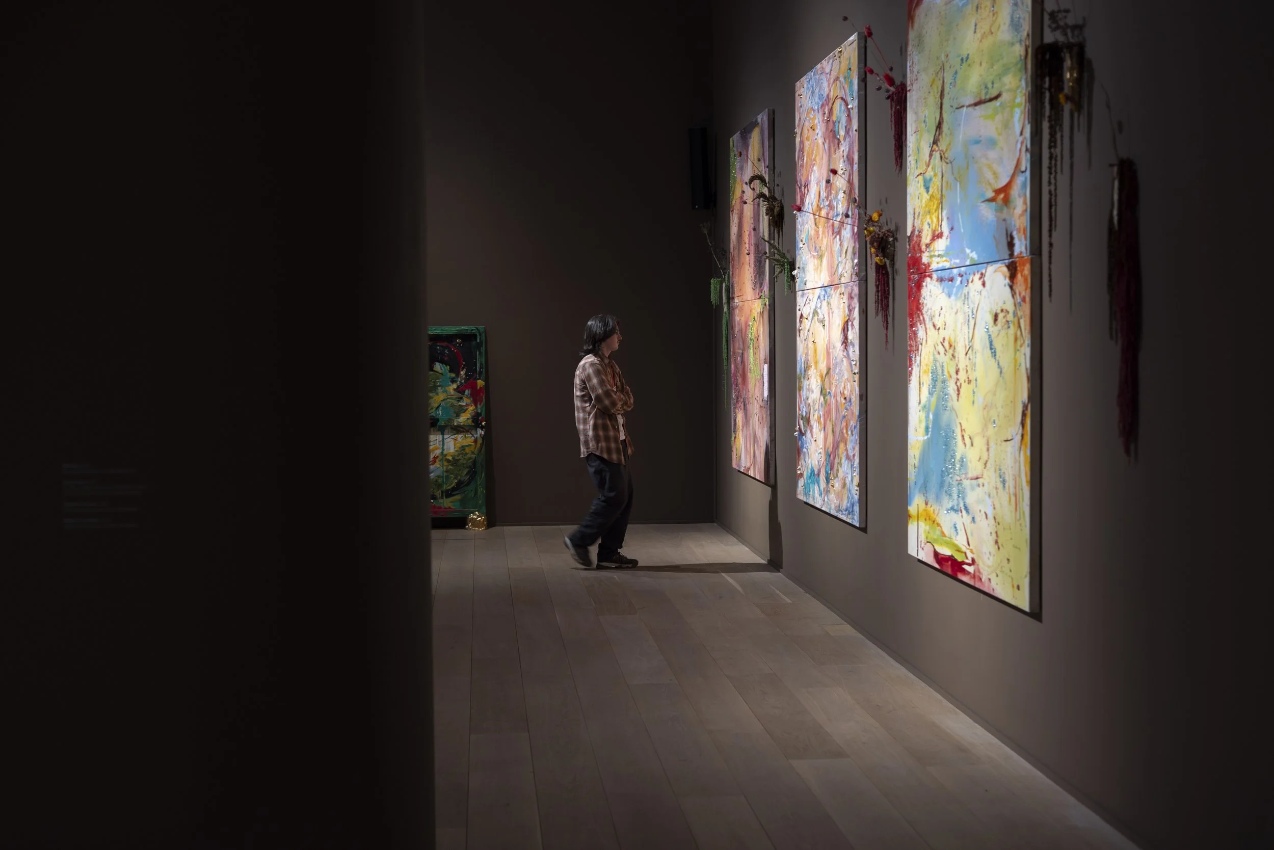 Young man standing in front of three large abstract canvases in exhibition space.