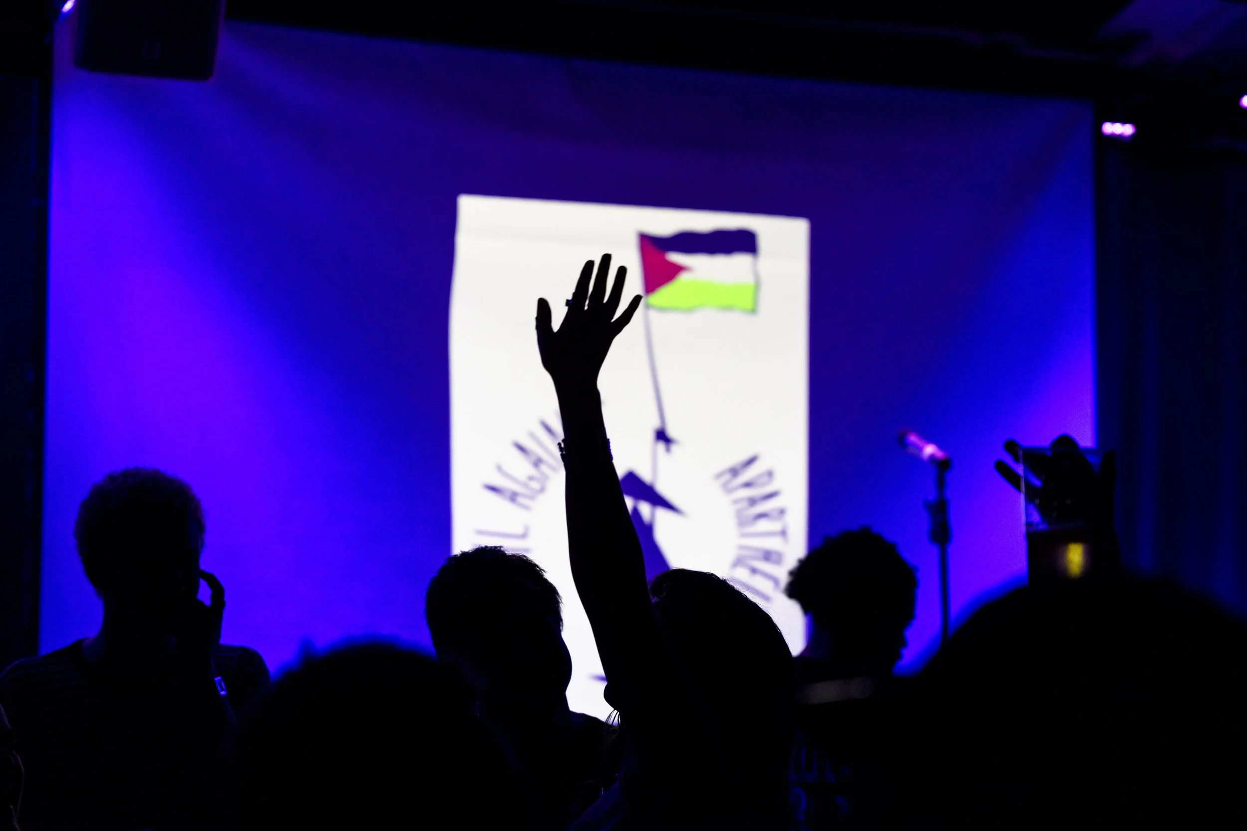 Silhouetted hand raised on dancefloor reaching toward projected Palestinian flag at Manchester event