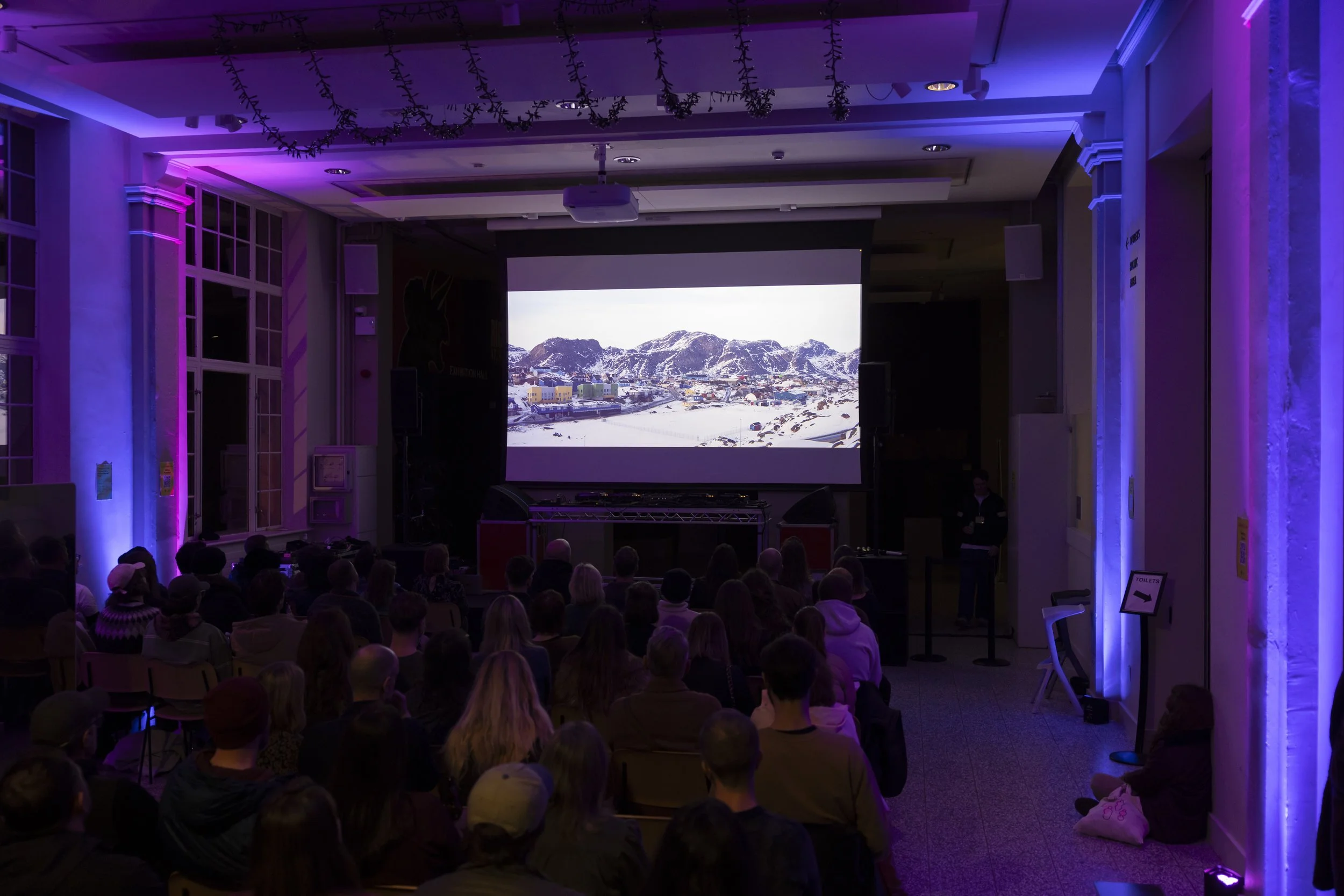 Audience watching TAKKUUK film screening inside gallery space at EarthSonic Live, Manchester Museum