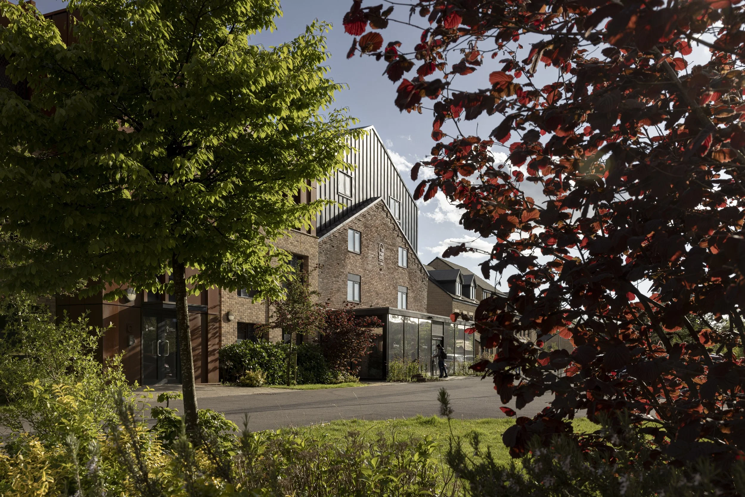 Front exterior of The Pump House by Just H Architects seen through foliage at dusk light in Lancaster