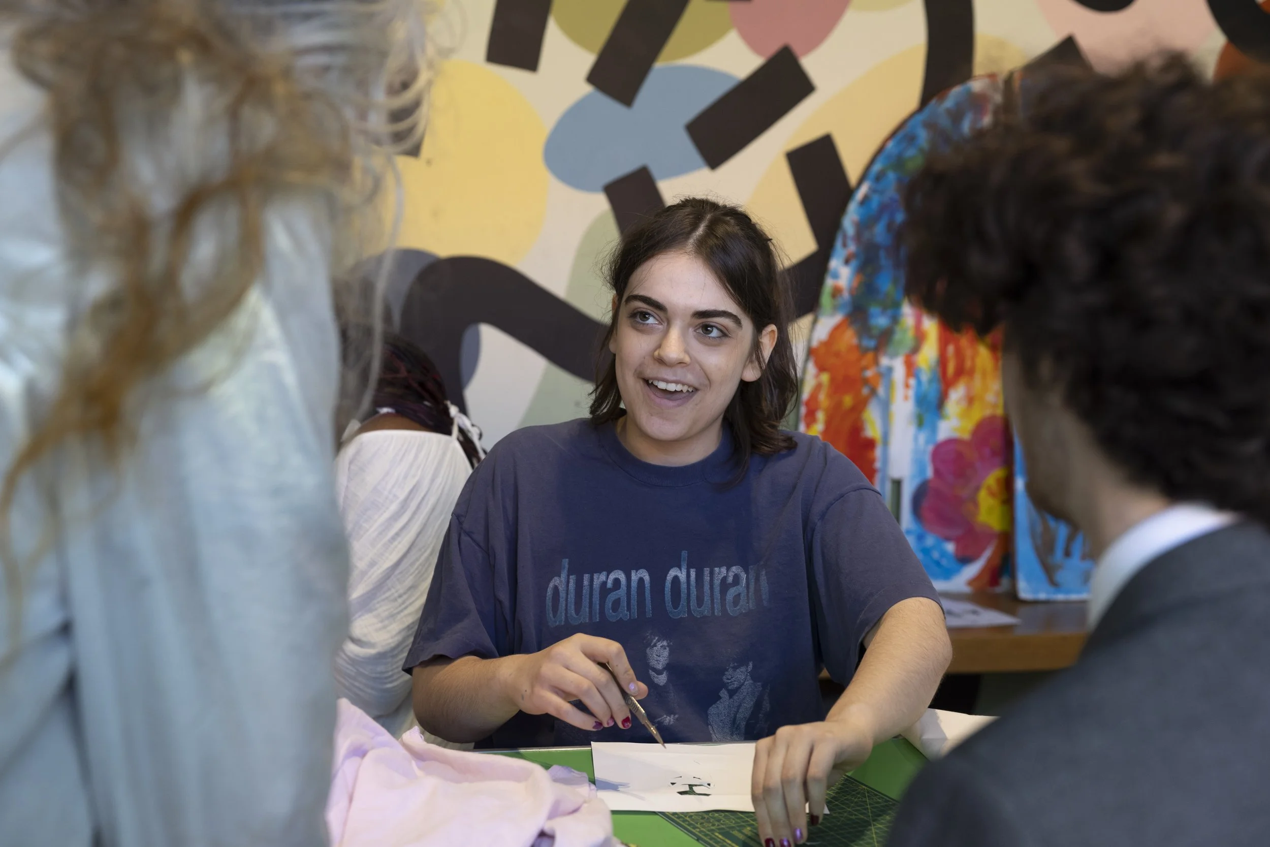 Young student cutting a stencil while speaking with Delaine Le Bas during an upcycling workshop at The Whitworth, Manchester, collaborative textile and mixed-media art practice