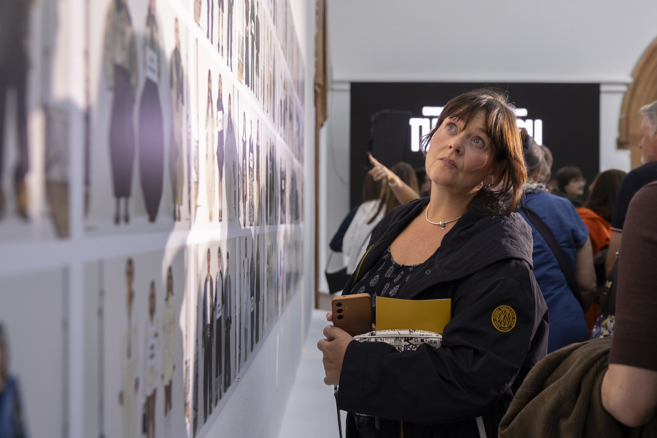 Audience member viewing printed exhibition work displayed on a wall during Manchester Fashion Institute fashion showcase at Manchester Metropolitan University.
