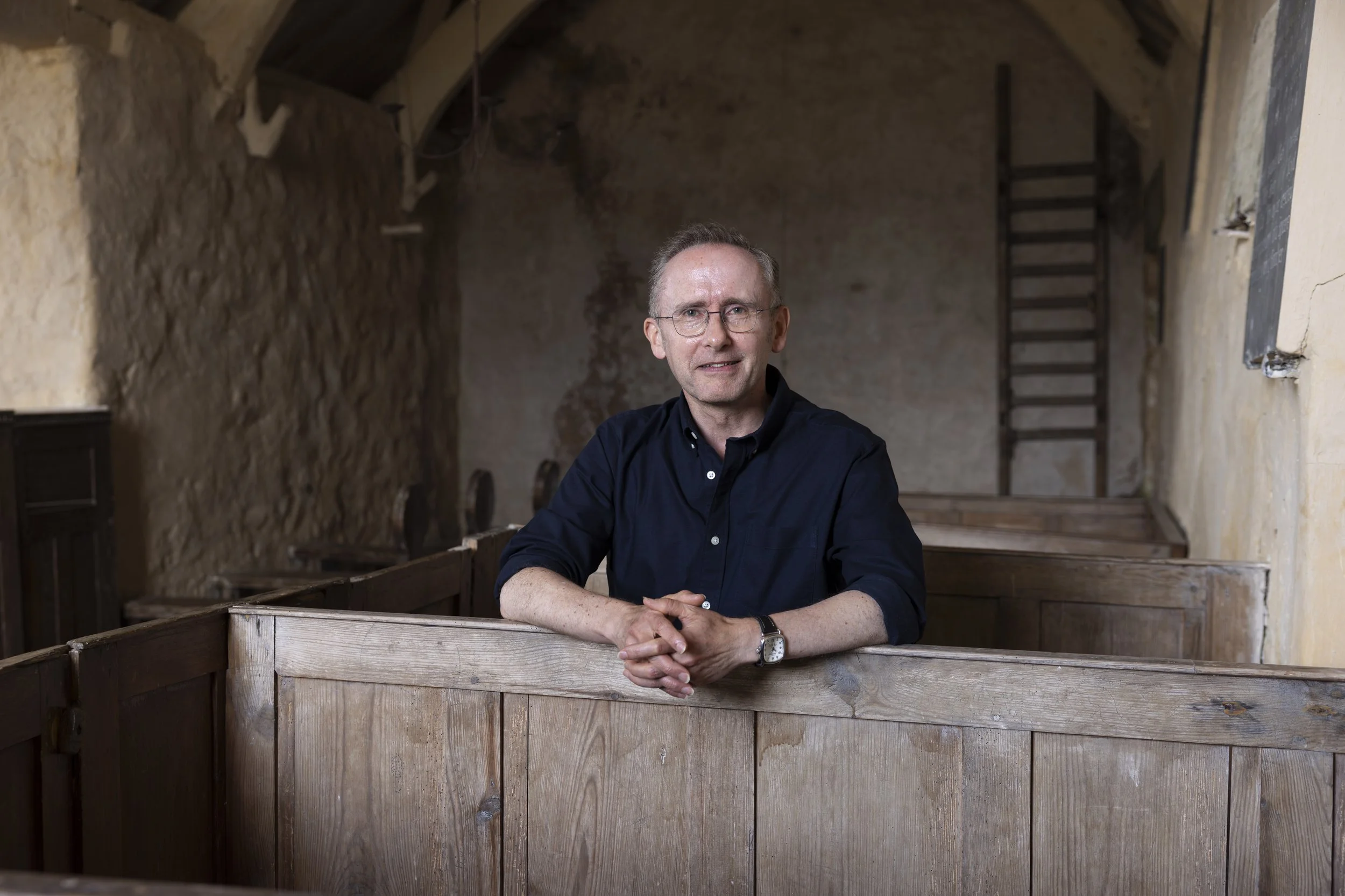 David Farrington sitting in a box pew at St Baglan’s Church, looking towards the camera.