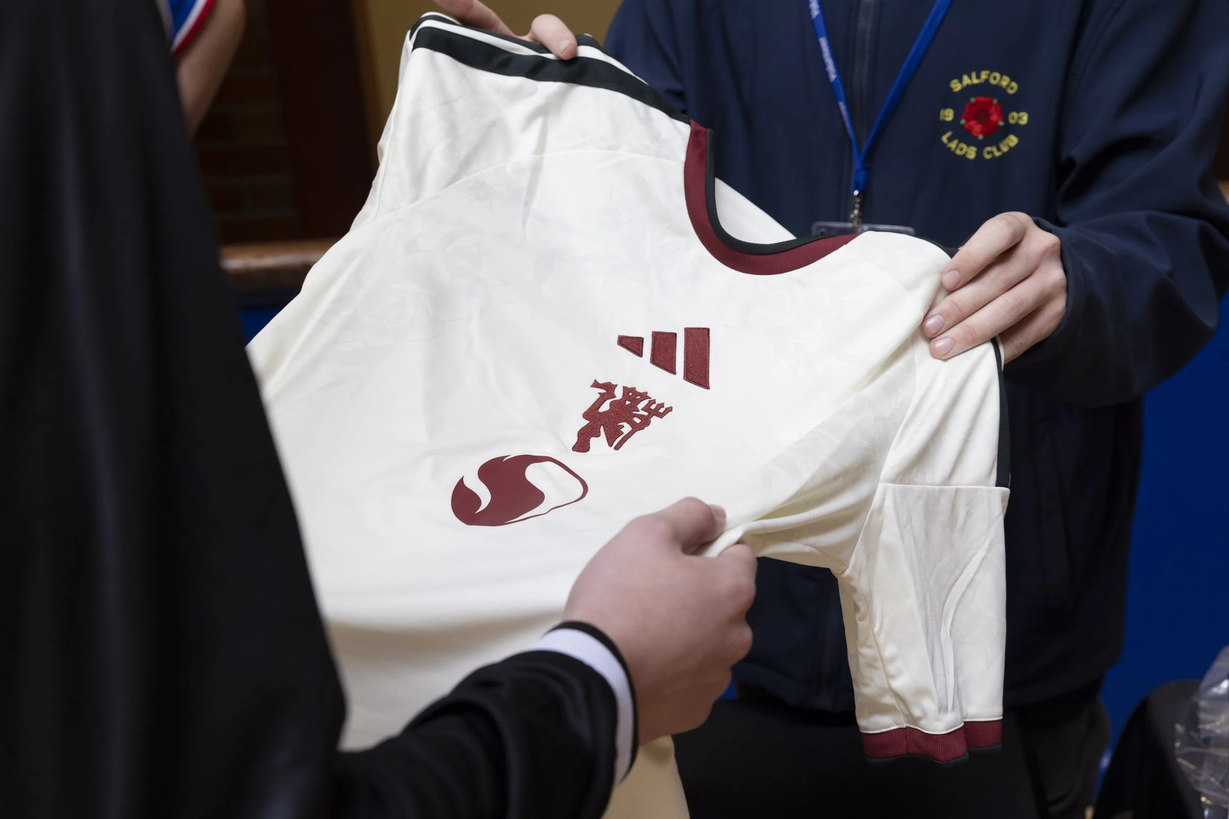 A customer and staff member hold the new Manchester United third shirt between them in a pub, with the adidas and Manchester United badges visible.