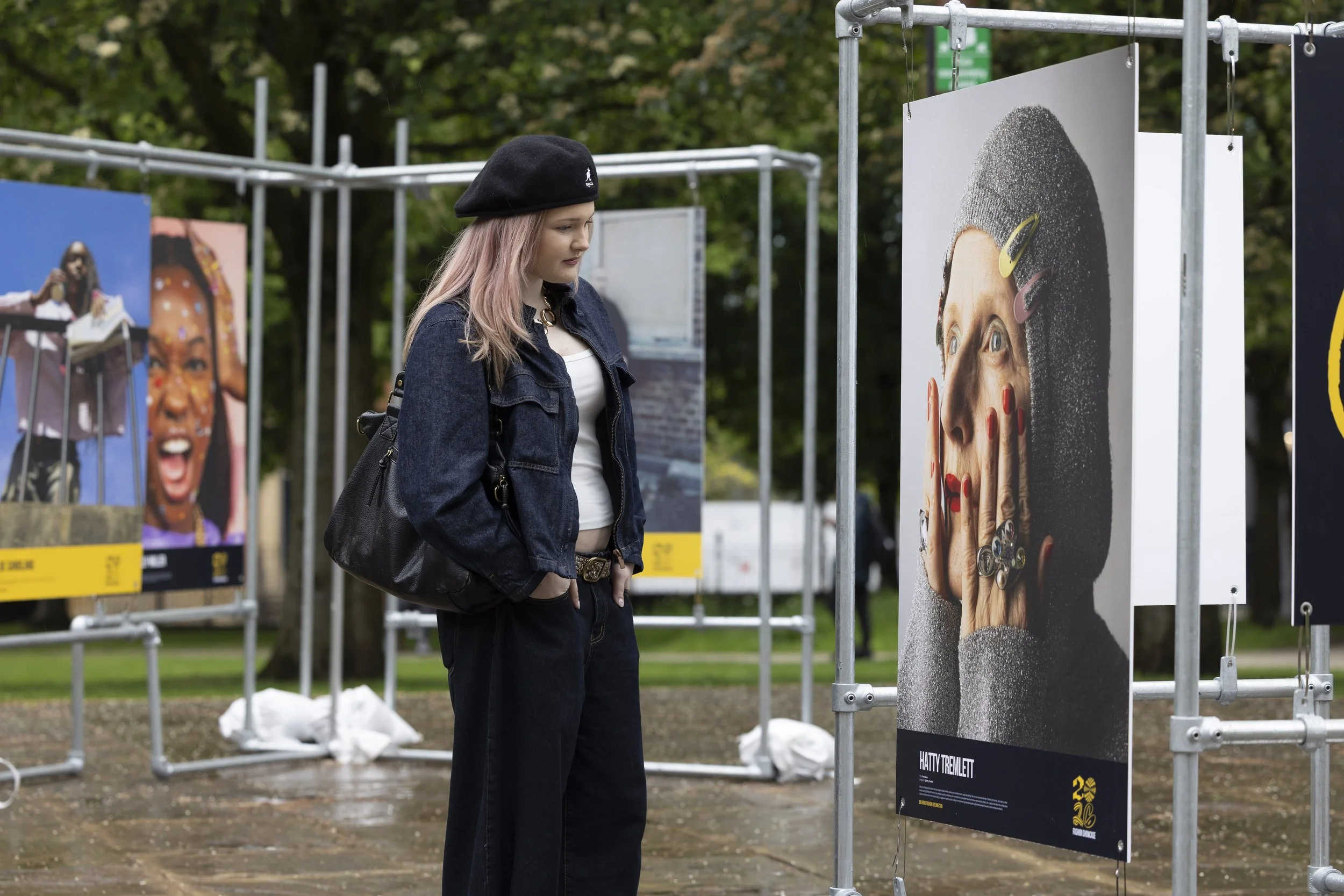 Visitor examining large-scale printed fashion photographs displayed on outdoor banners at Manchester fashion showcase exhibition space.