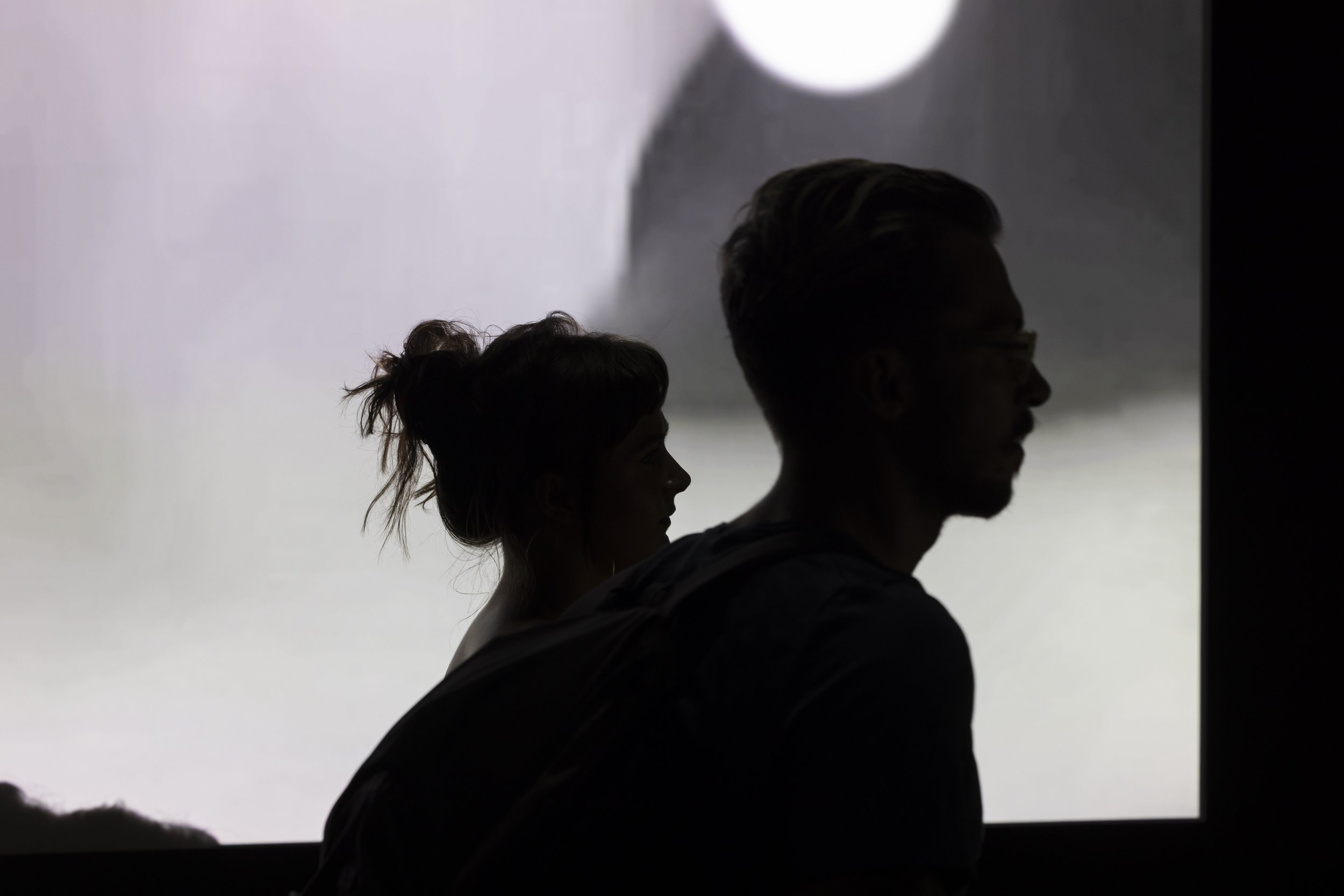 Two people silhouetted against a video artwork at Manchester Metropolitan University's More to Come postgraduate degree show.