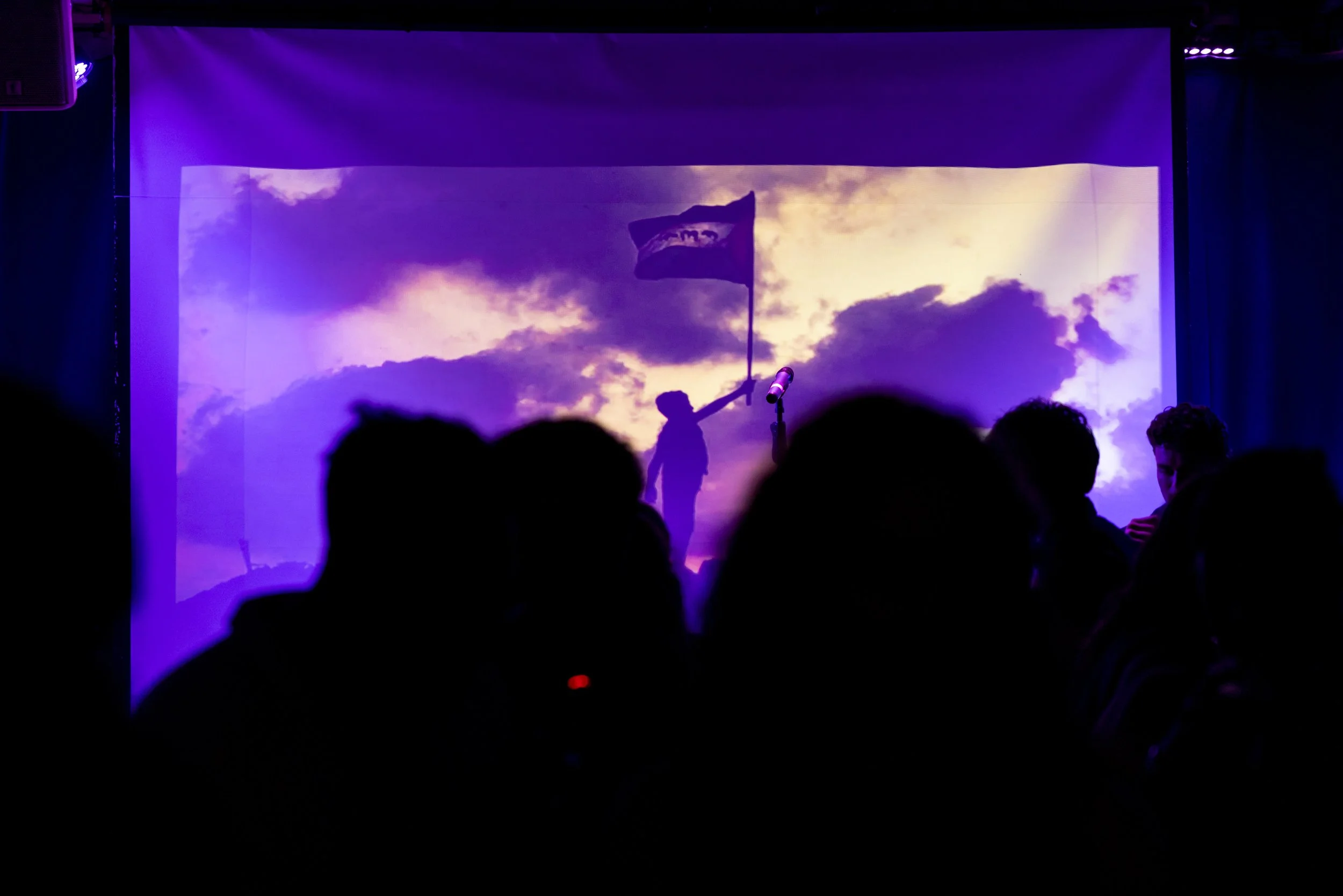 Crowd watching projected image of child holding Palestinian flag at live music fundraiser in Manchester