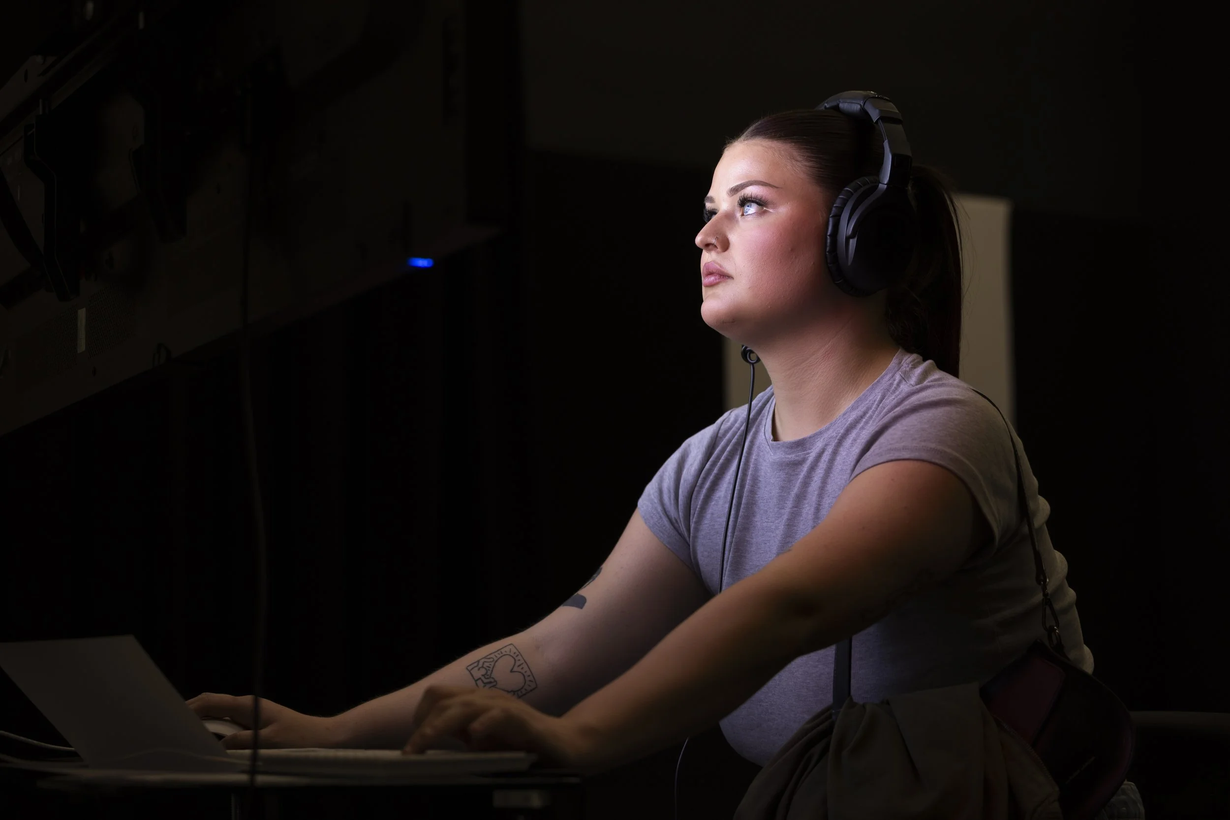Young woman wearing headphones and illuminated by a video screen at Manchester Metropolitan University's More to Come postgraduate art exhibition.