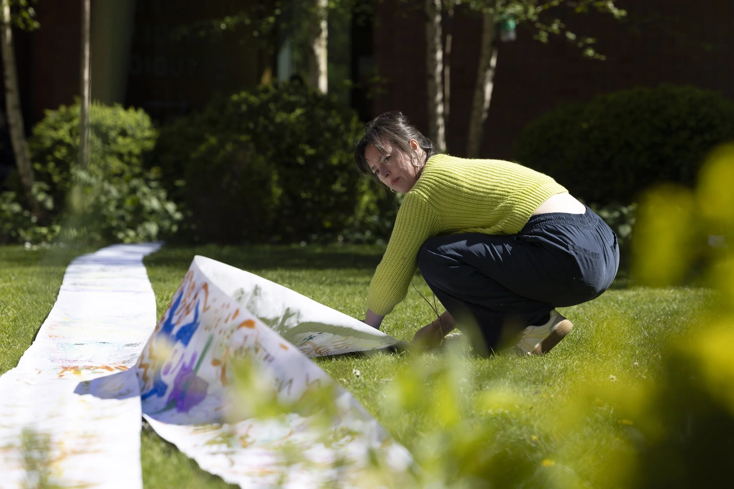 Participant laying out a long paper artwork on the grass in Whitworth Park, Manchester, part of a process-led textile and mixed-media workshop