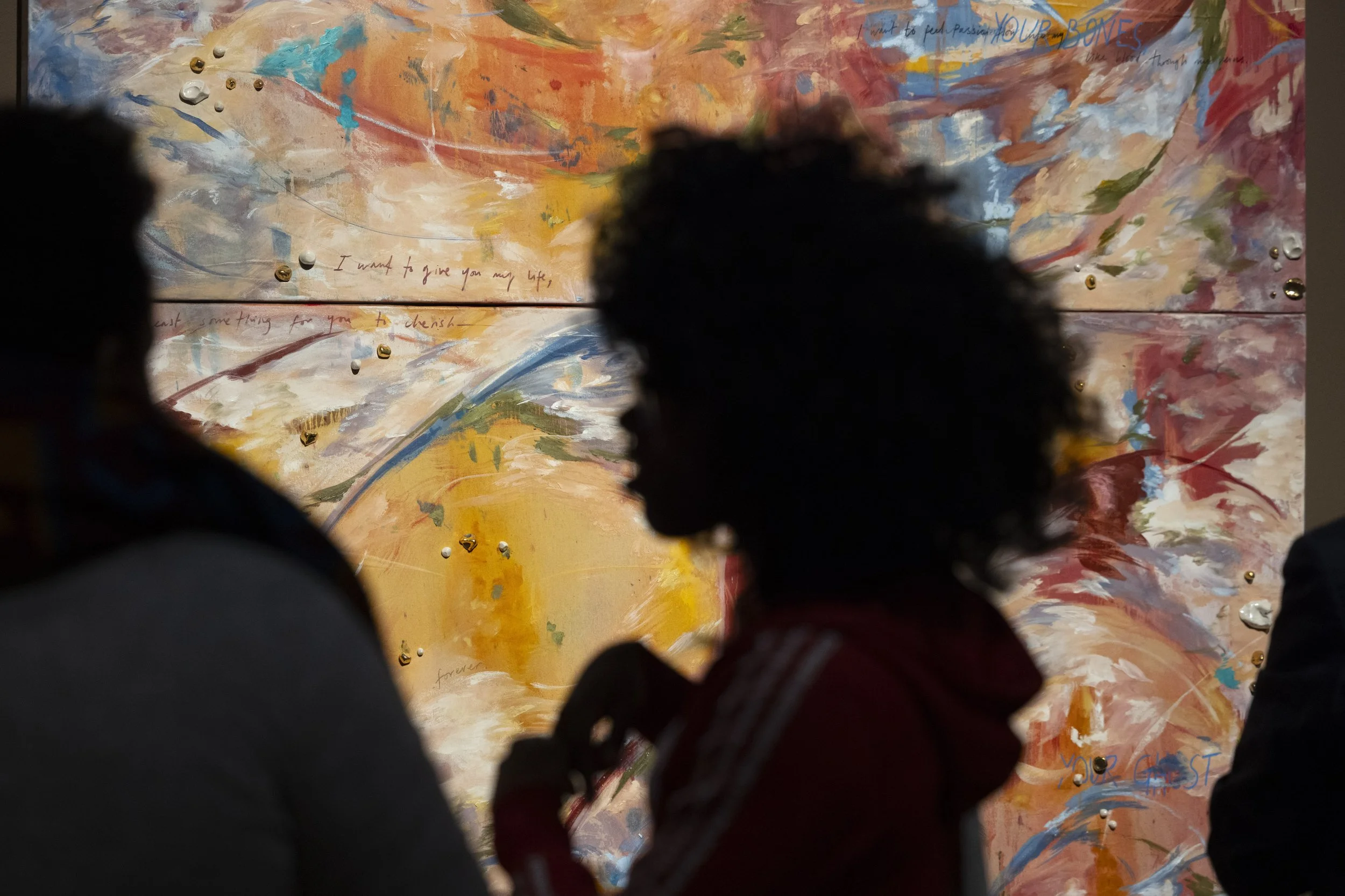 Young woman silhouetted against large colourful painting in contemporary gallery exhibition.