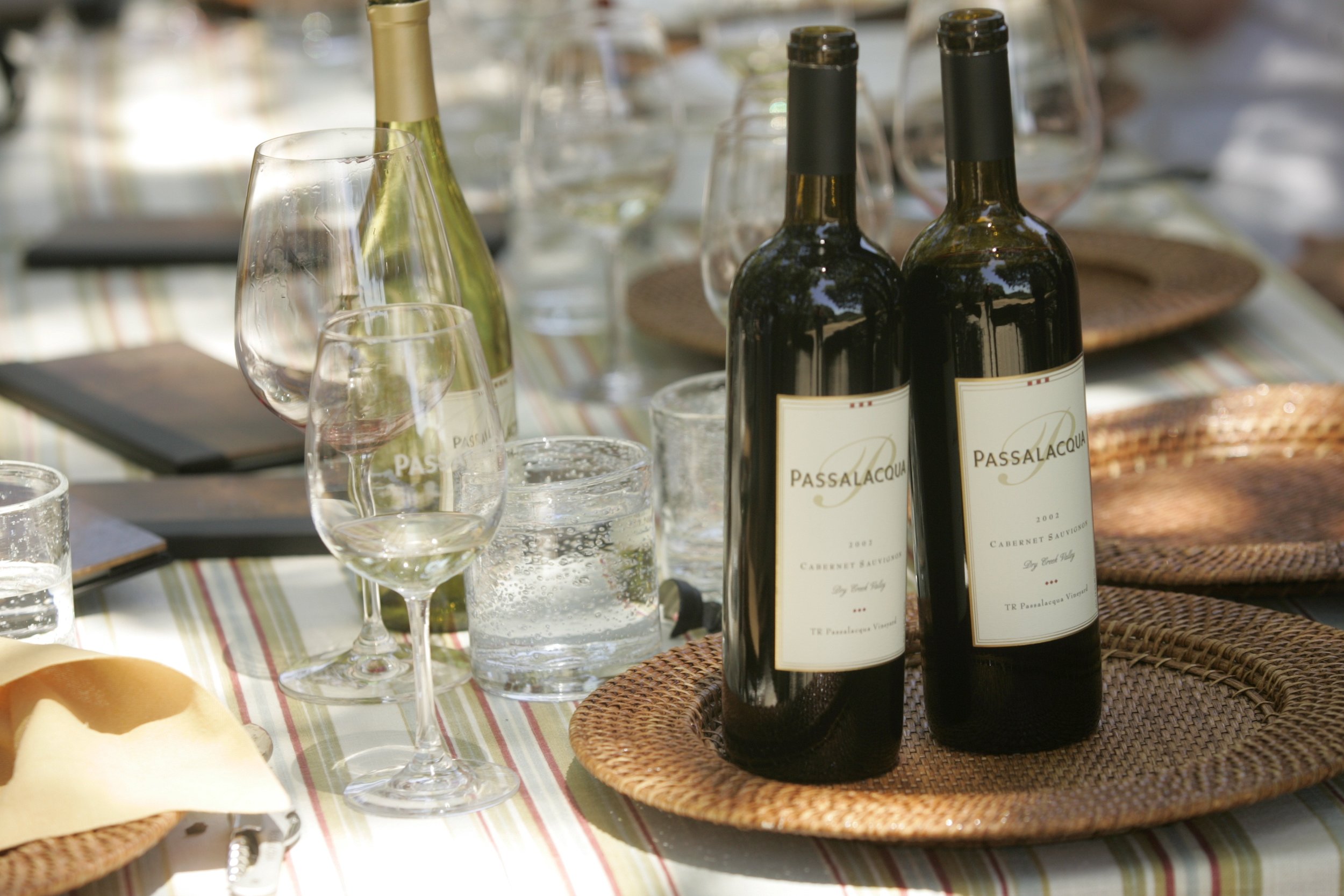 2 bottles of red wine and one bottle of white on table with wine glasses