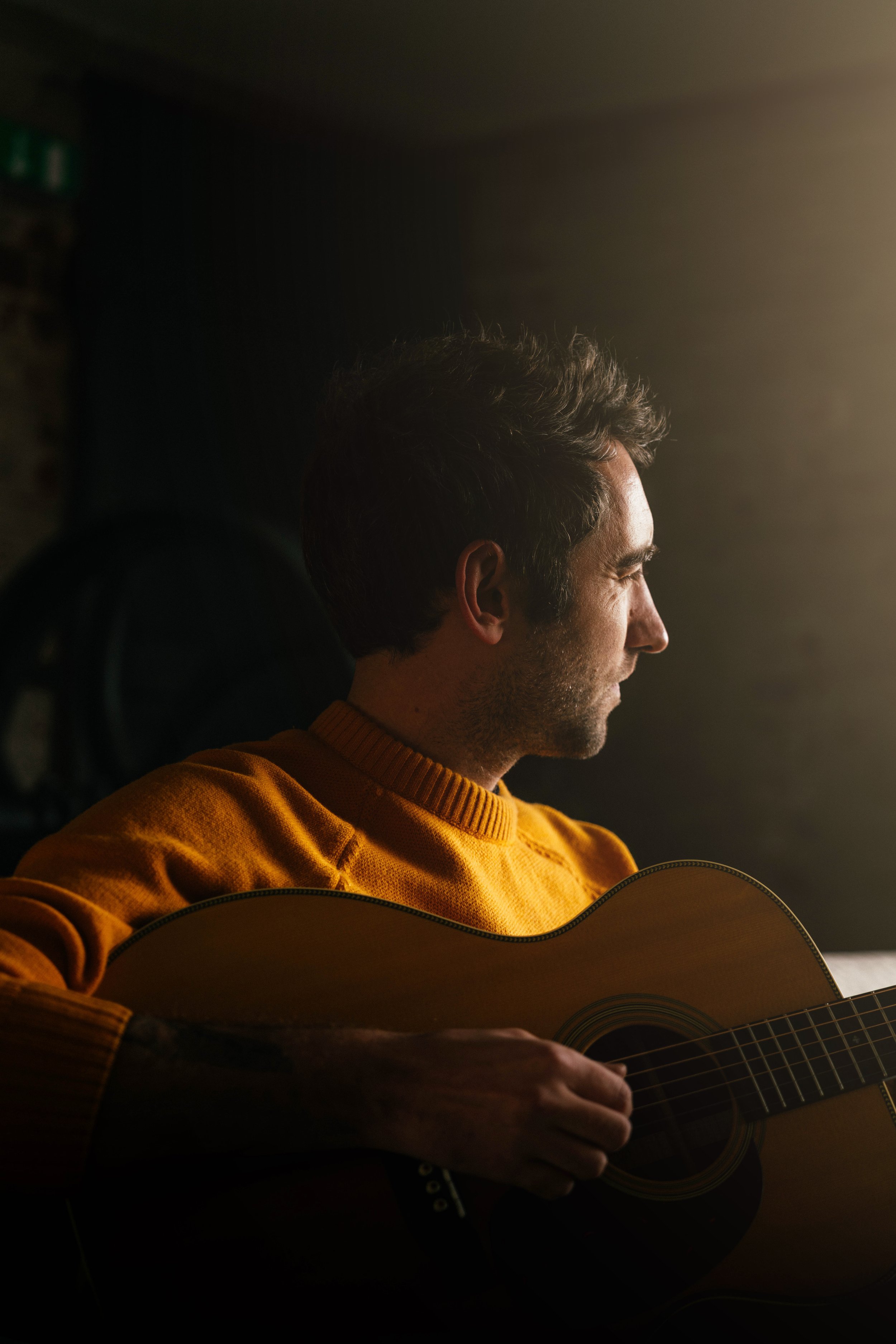 Musician playing acoustic guitar in warm golden light — moody music portrait photography