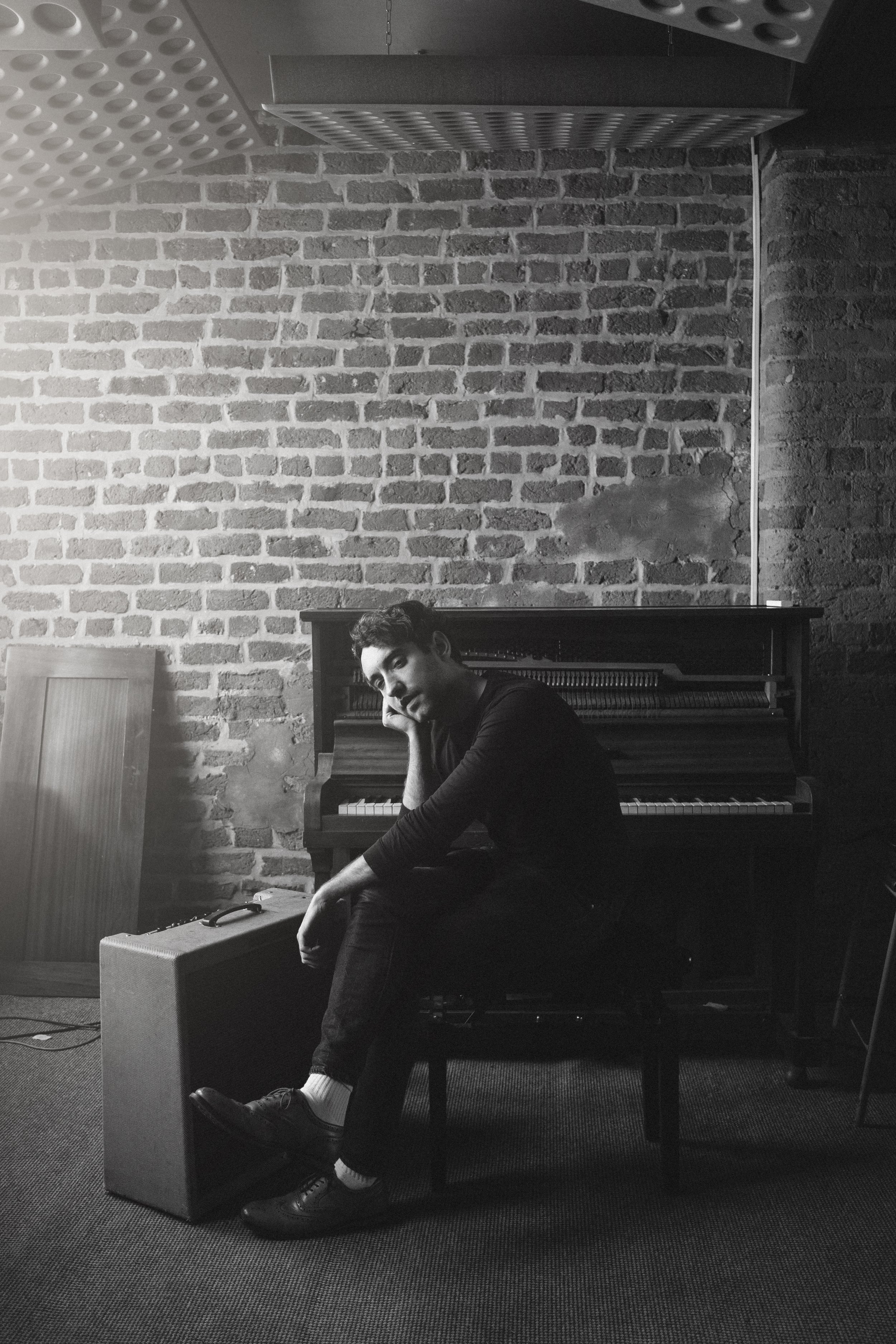 Musician at upright piano in brick-walled room — atmospheric music photography