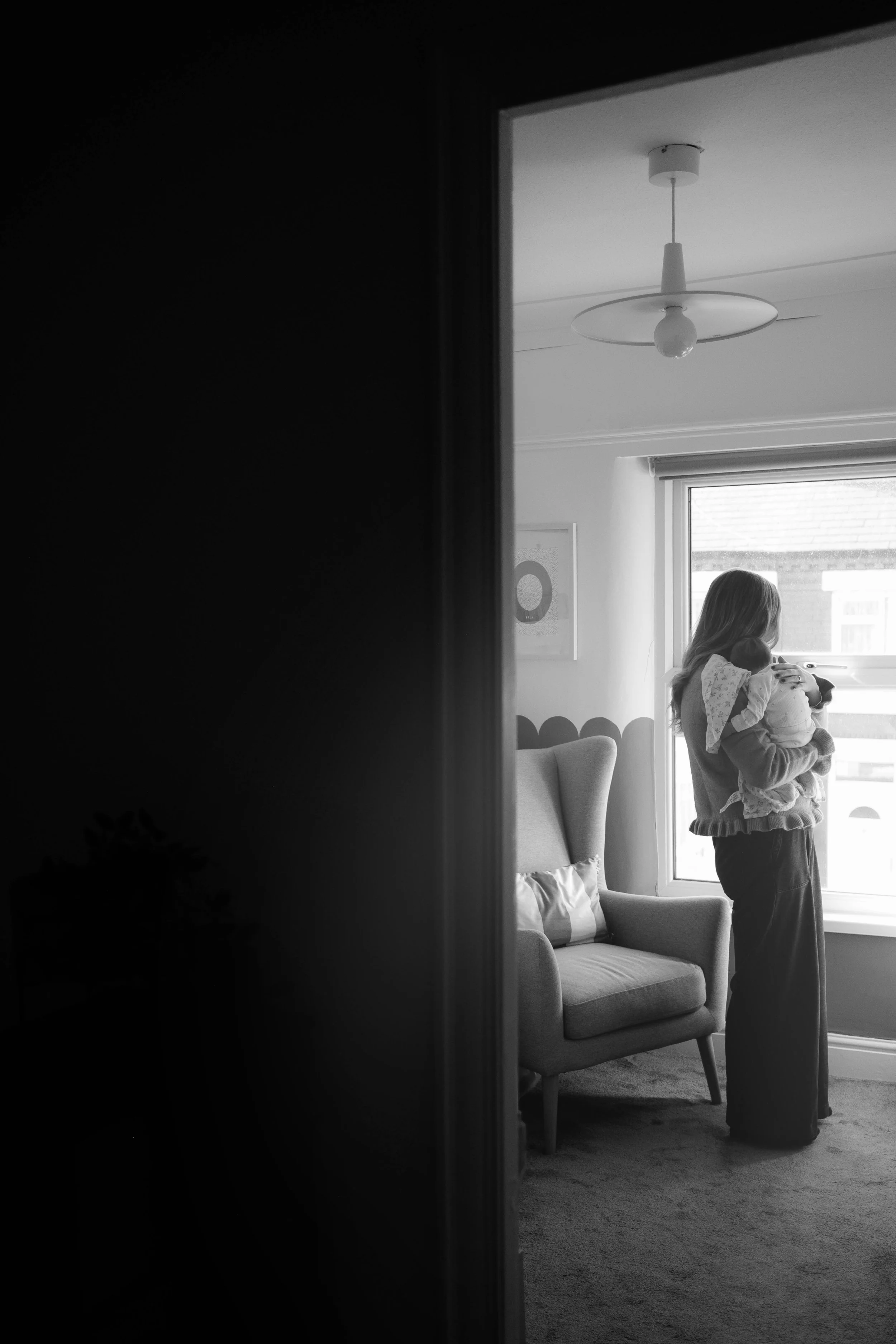 Person sitting alone in a dark room by the window — moody atmospheric portrait photography