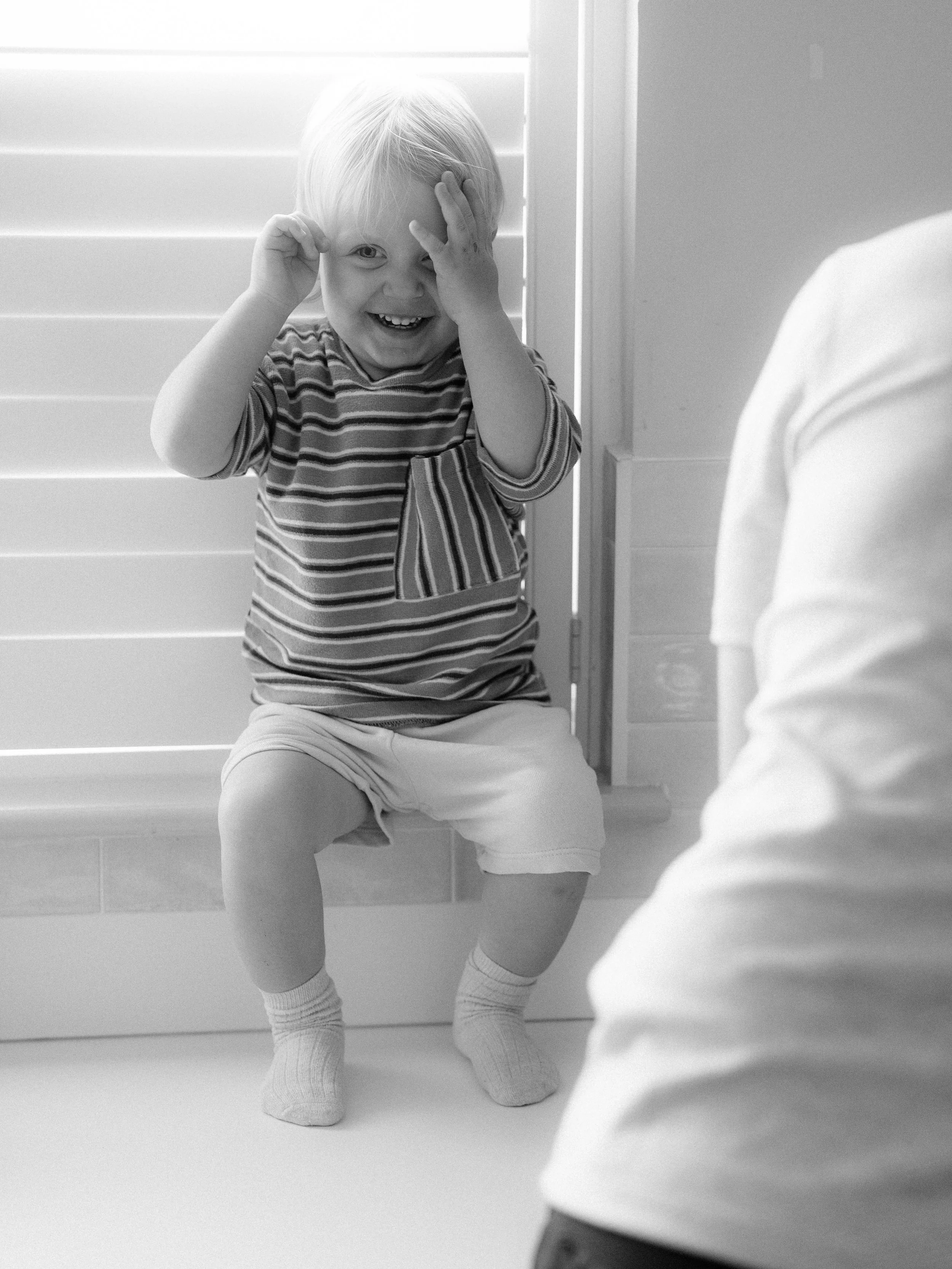Child sitting on stairs looking up playfully — candid family portrait photography