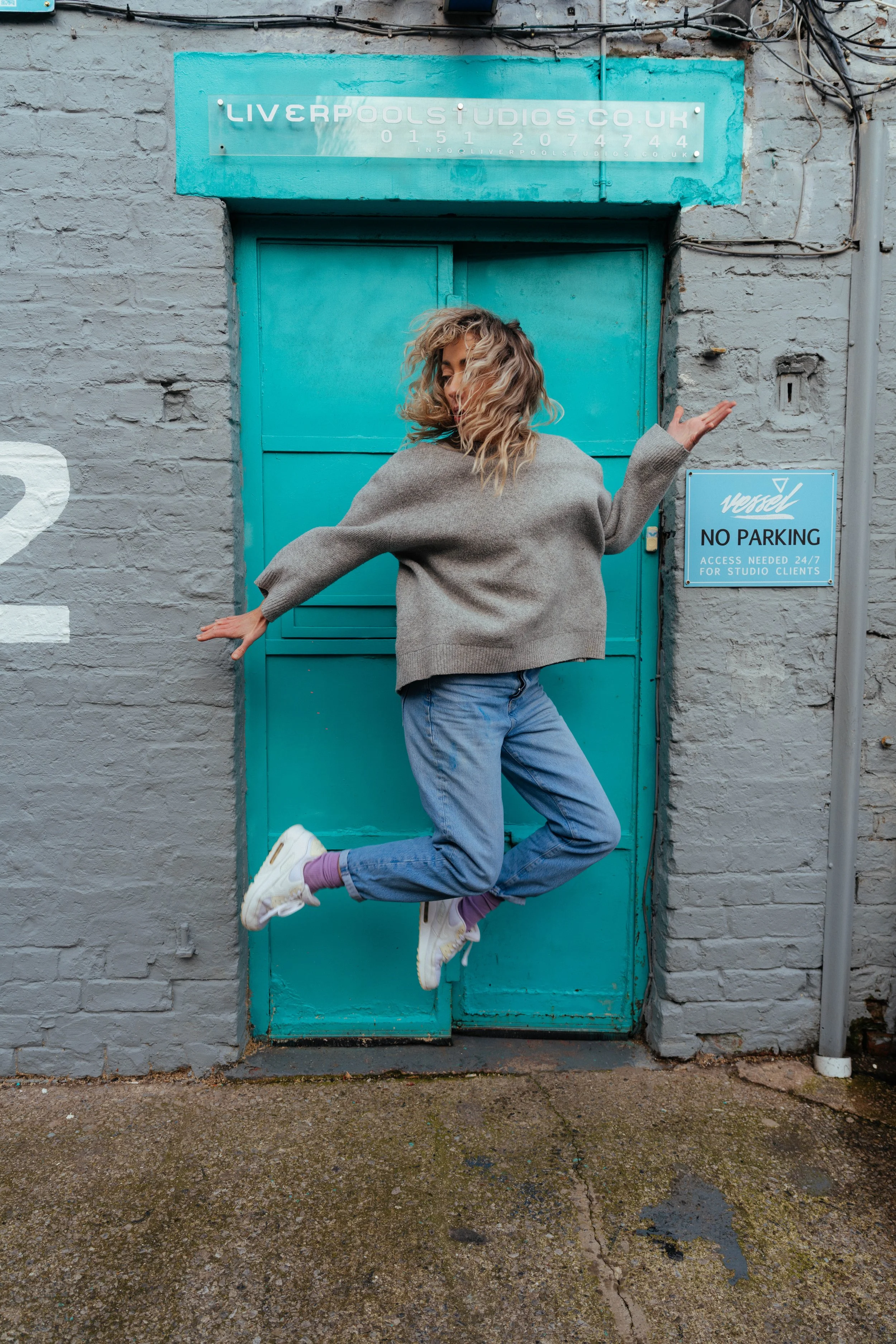Fun location portrait — woman jumping in front of teal door, urban street photography