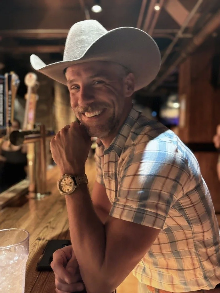 Craig Klonowski smiling in a cowboy hat at a warmly lit New York bar.