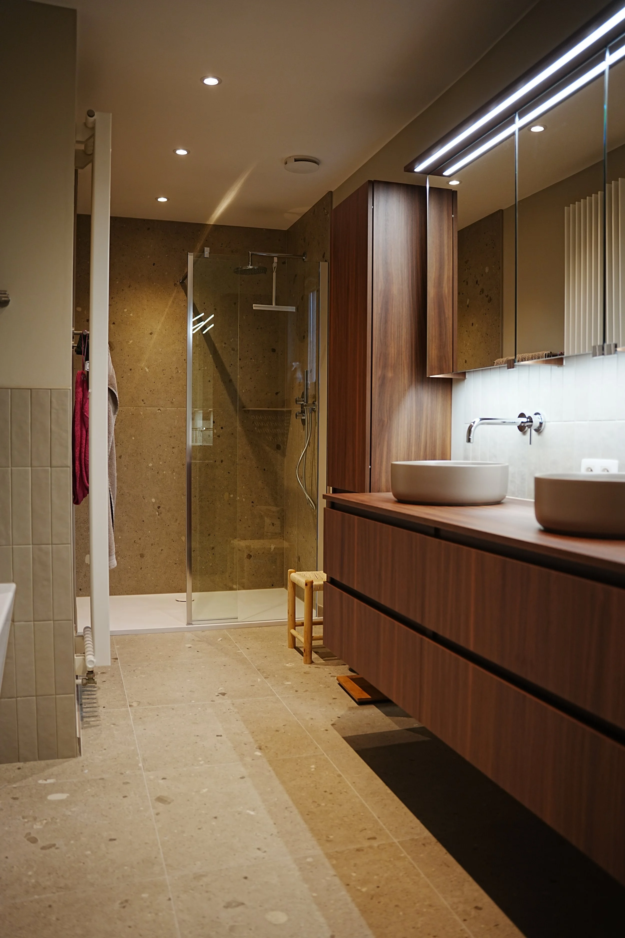 Moderne badkamer met dubbele wasbakken, grote spiegel, houten kastjes en inloopdouche met glazen deur.