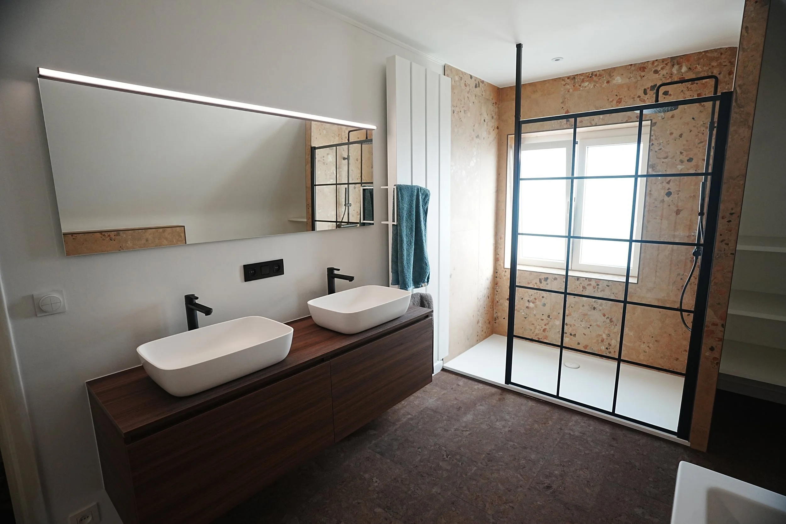 Moderne badkamer met dubbele wasbakken, groot horizontaal spiegel, inloopdouche met glazen wand, raam en strakke zwarte kranen.