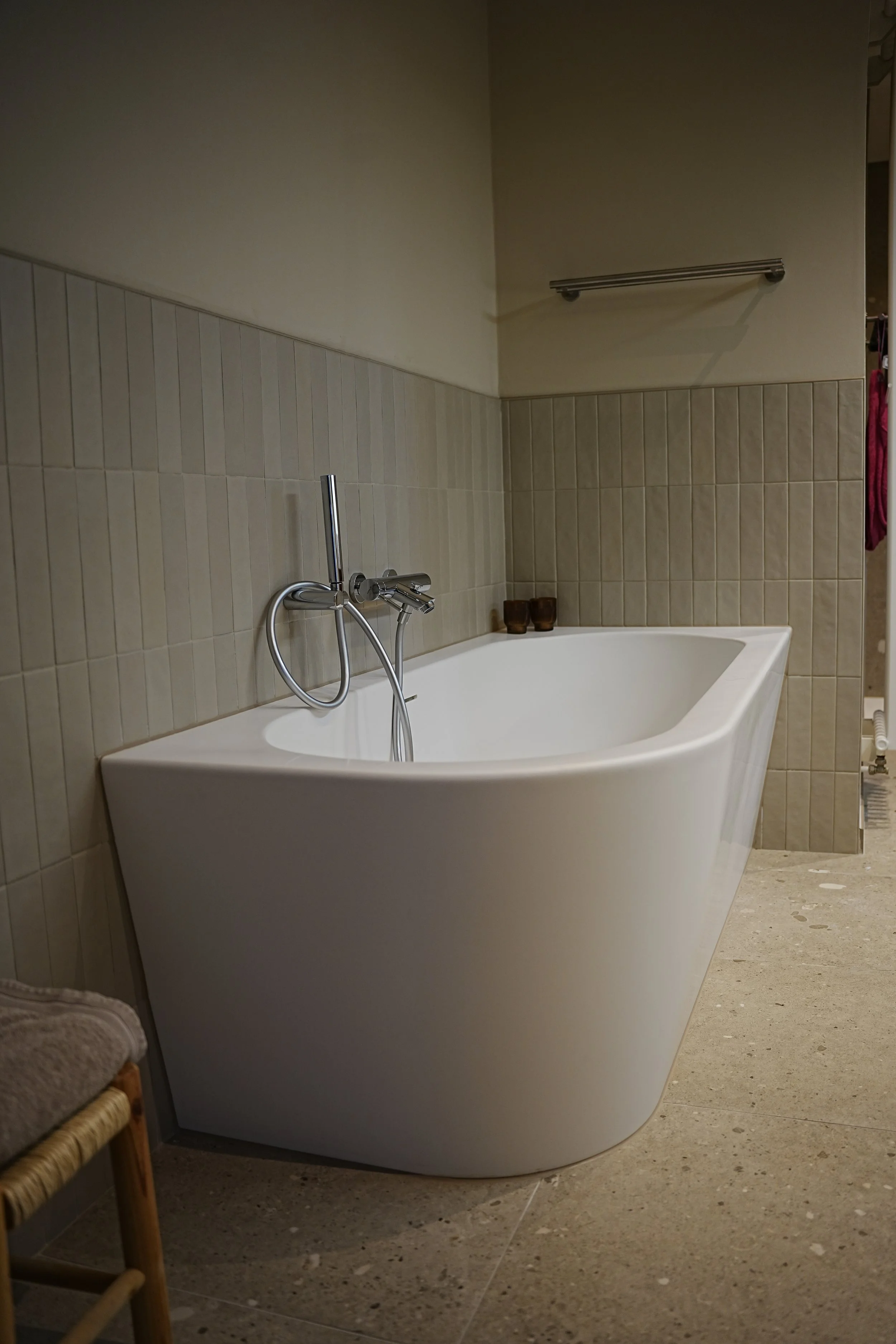 Een moderne vrijstaande badkuip in een badkamer met beige betegelde muren en een betonnen vloer.