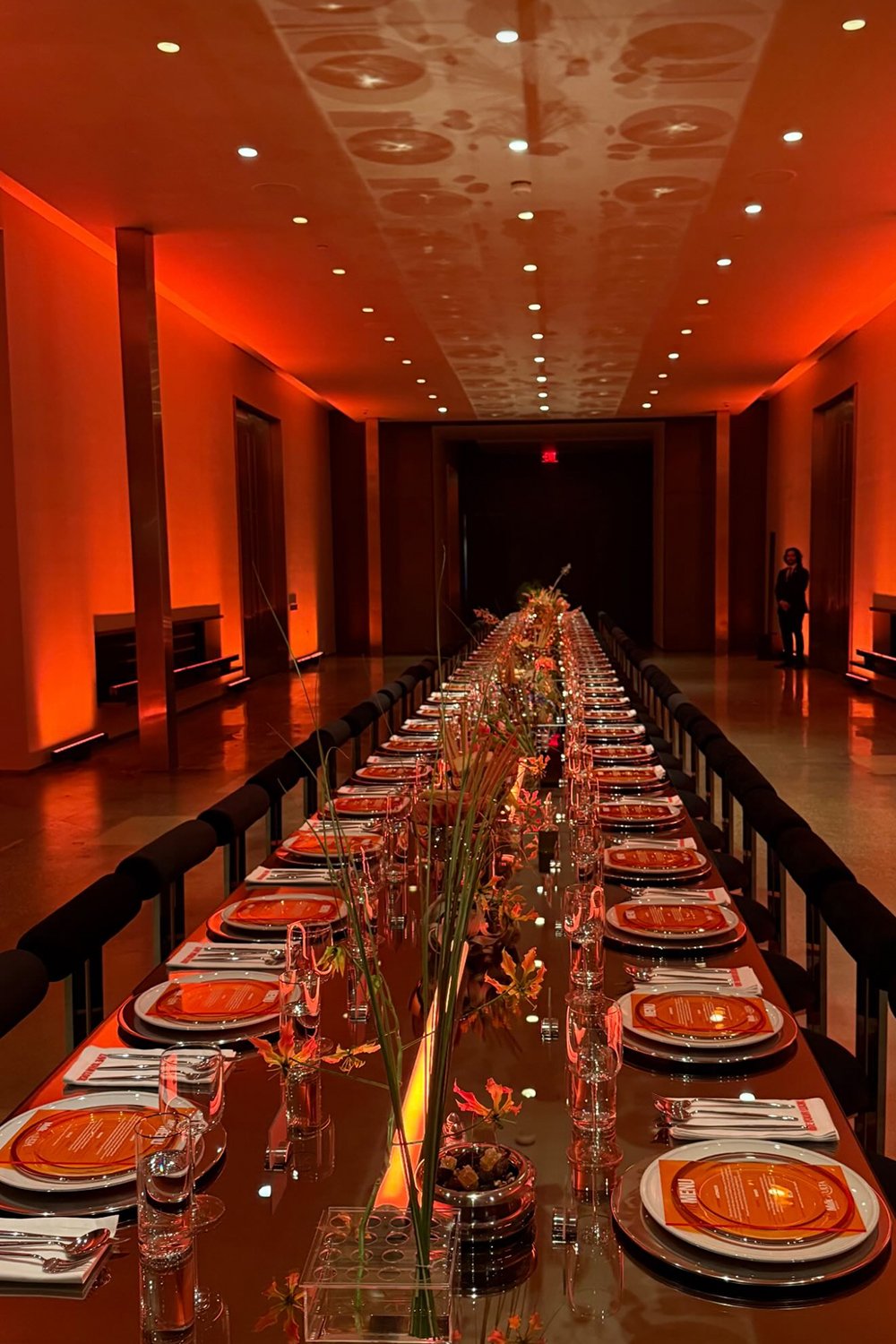 Long mirrored dinner table set for the Milk Makeup x Ulta Beauty launch party at Milk Studios Los Angeles, catered by Cava & Cake. Elegant table setting with bold orange menus, clear glassware, and modern floral arrangements reflecting California-It