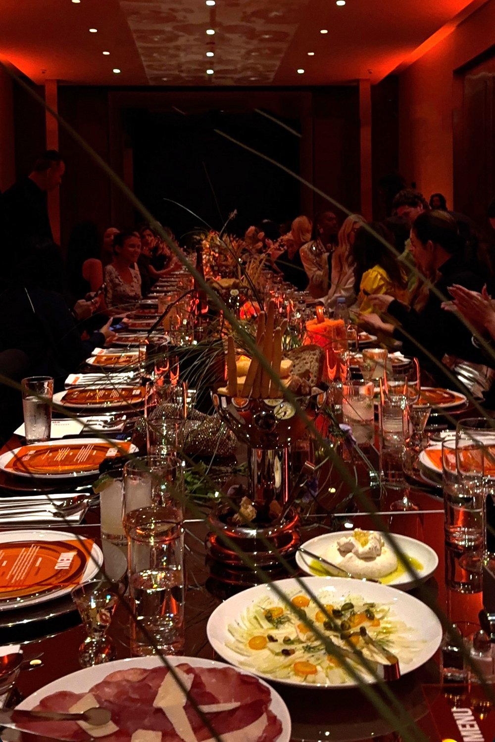 Guests seated at a vibrant, candlelit dinner table during the Milk Makeup x Ulta Beauty event at Milk Studios in Los Angeles, with colorful antipasto plates of burrata, bresaola, and fennel-kumquat carpaccio displayed in the foreground.