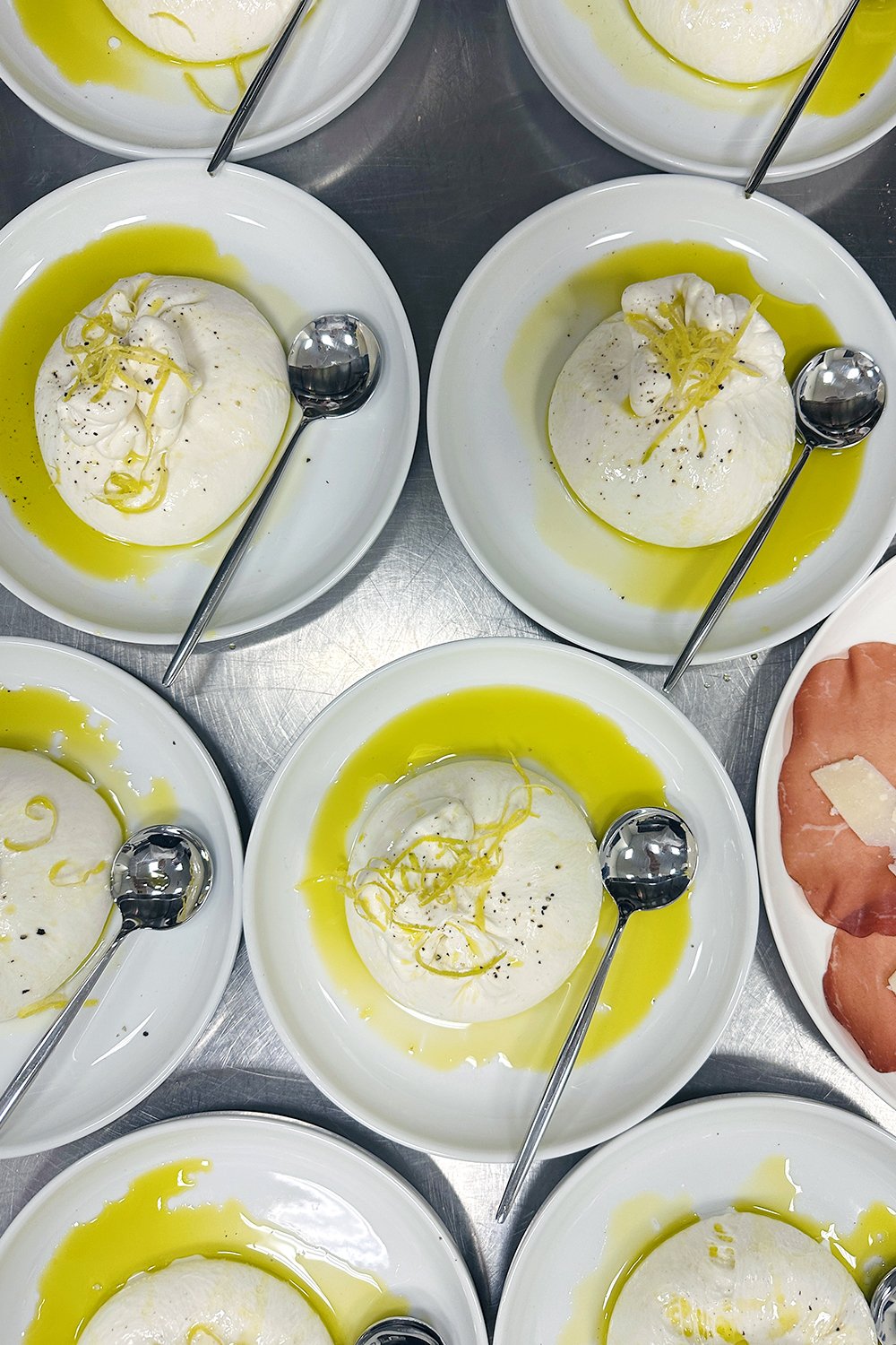 Individual servings of creamy burrata drizzled with extra virgin olive oil and topped with lemon zest and cracked pepper, prepared by Cava & Cake for the Milk Makeup x Ulta Beauty dinner at Milk Studios in Los Angeles.