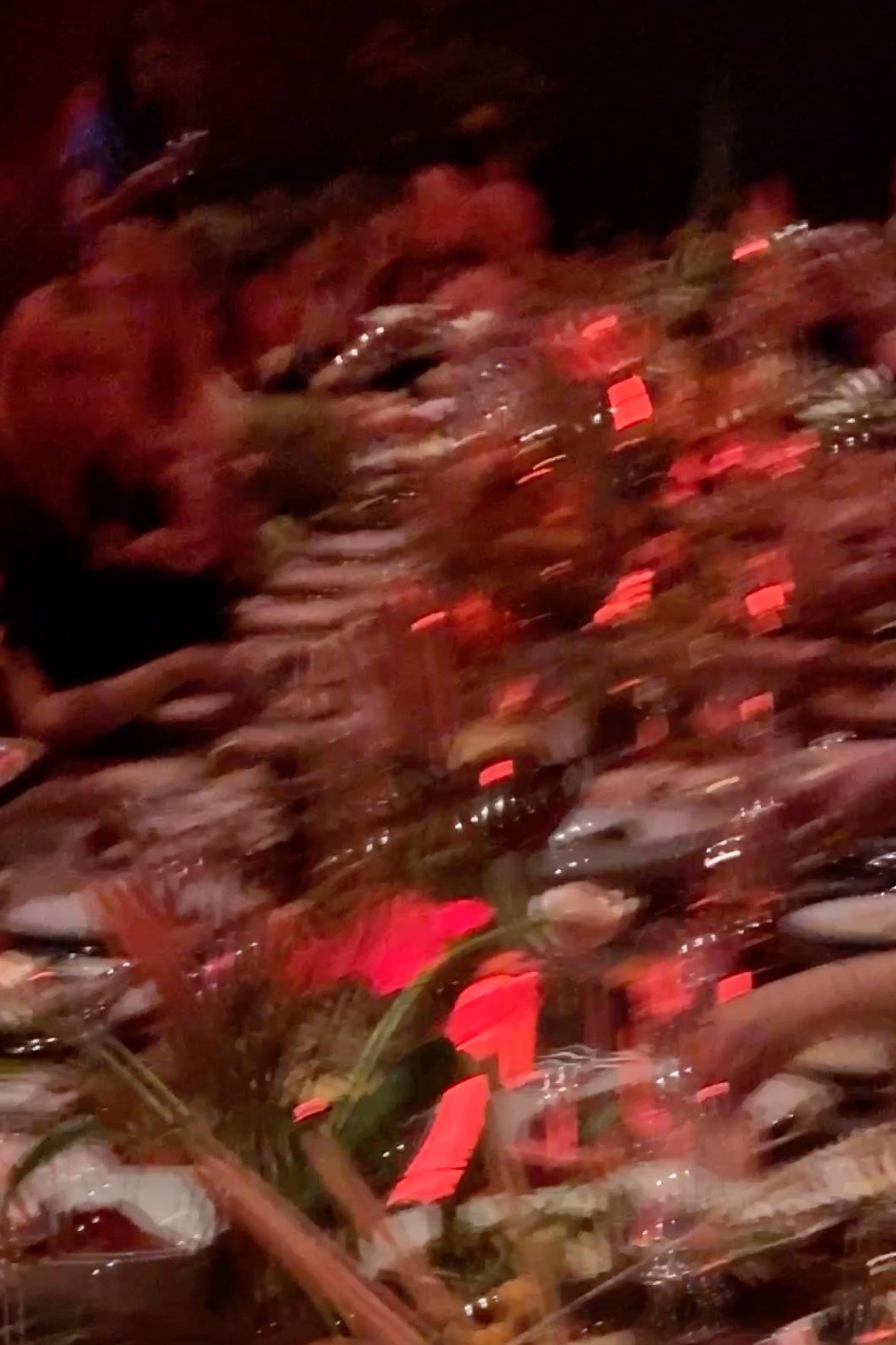 Artful, motion-blurred photo of guests gathered around a long, flower-adorned dinner table at the Milk Makeup x Ulta Beauty event at Milk Studios in Los Angeles. The table is aglow with red-orange lighting, creating an atmospheric and vibrant party v