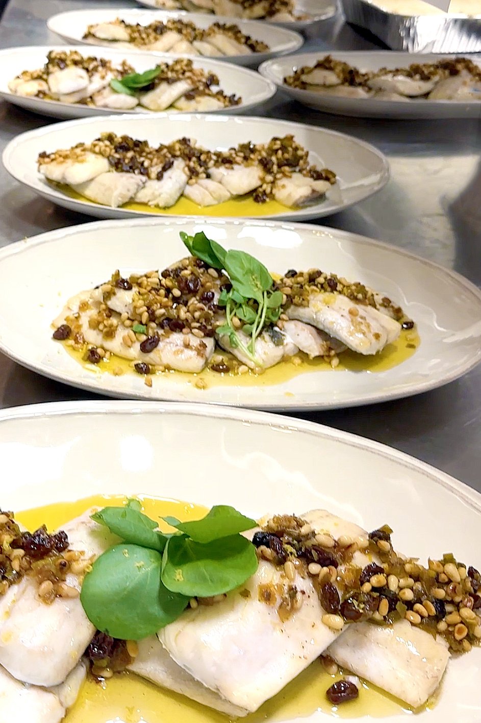 Plated branzino fillets topped with golden grappa-soaked raisin agrodolce and toasted pine nuts, finished with fresh lemon zest and herbs, prepared by Cava & Cake for the Milk Makeup x Ulta dinner.