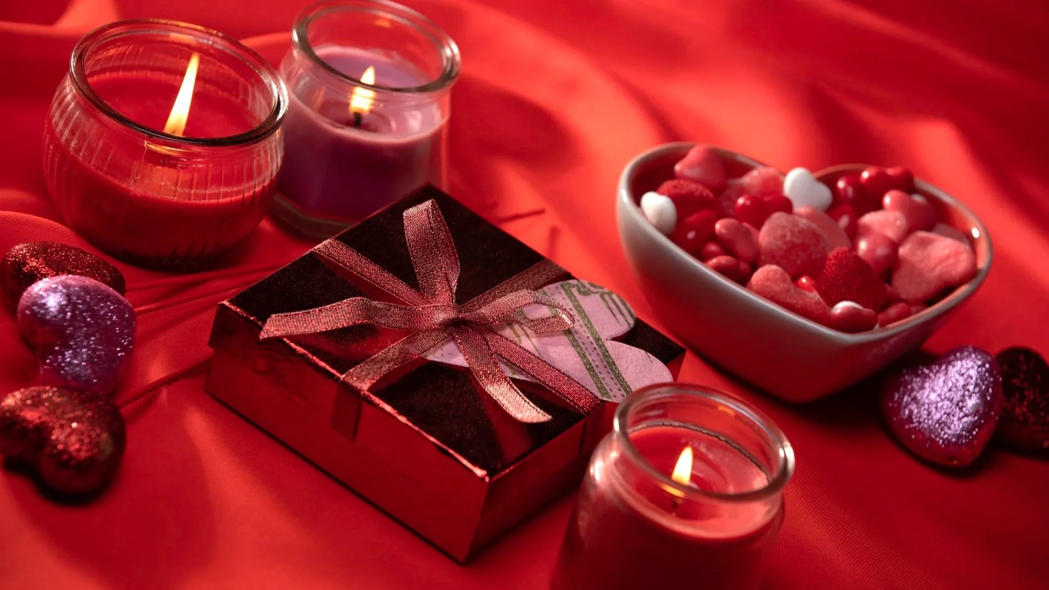 Photograph of candles, chocolate box, and candy bowl on a red table cloth.