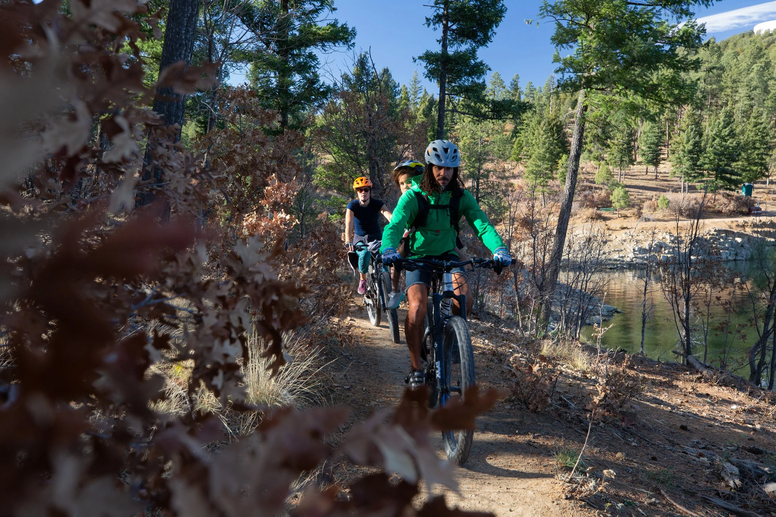A family rides mountain bikes along a scenic singletrack trail near Grindstone Lake in Ruidoso. Surrounded by towering pines and mountain landscapes, they enjoy one of the area’s popular outdoor adventures during the fall season.