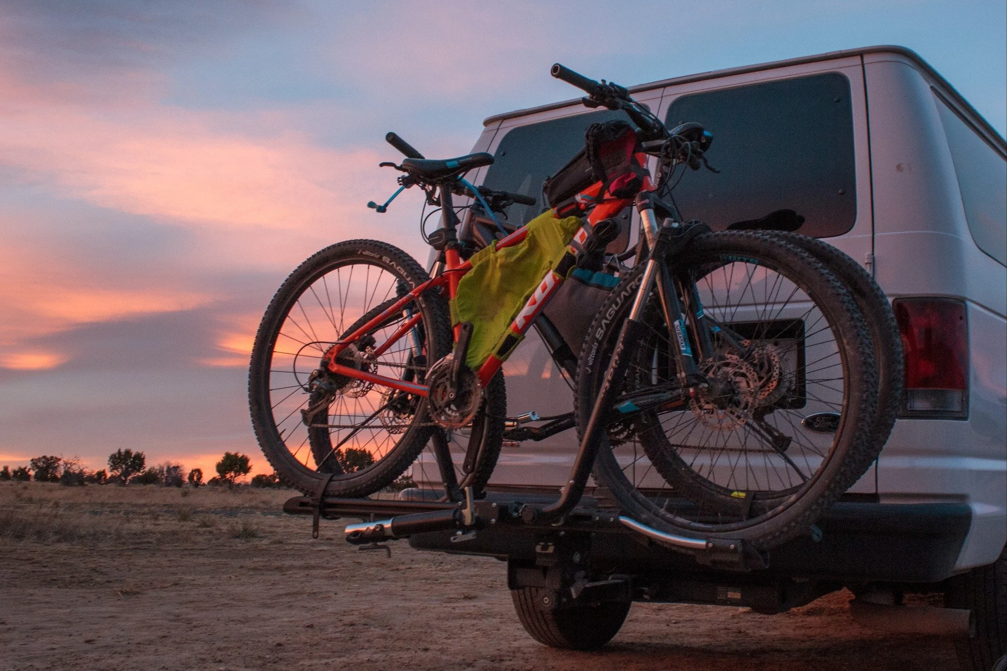 Two mountain bikes mounted on the back of a van at sunset, ready for an outdoor adventure.