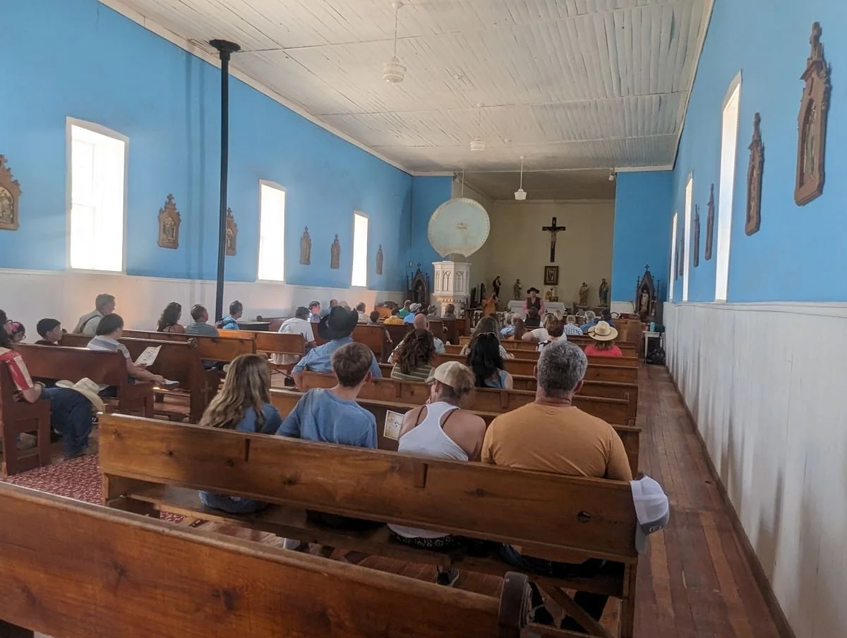 Visitors seated inside the historic San Juan Bautista Church in Lincoln, New Mexico, listening to a Lincoln Lecture Series presentation on Old West history.
